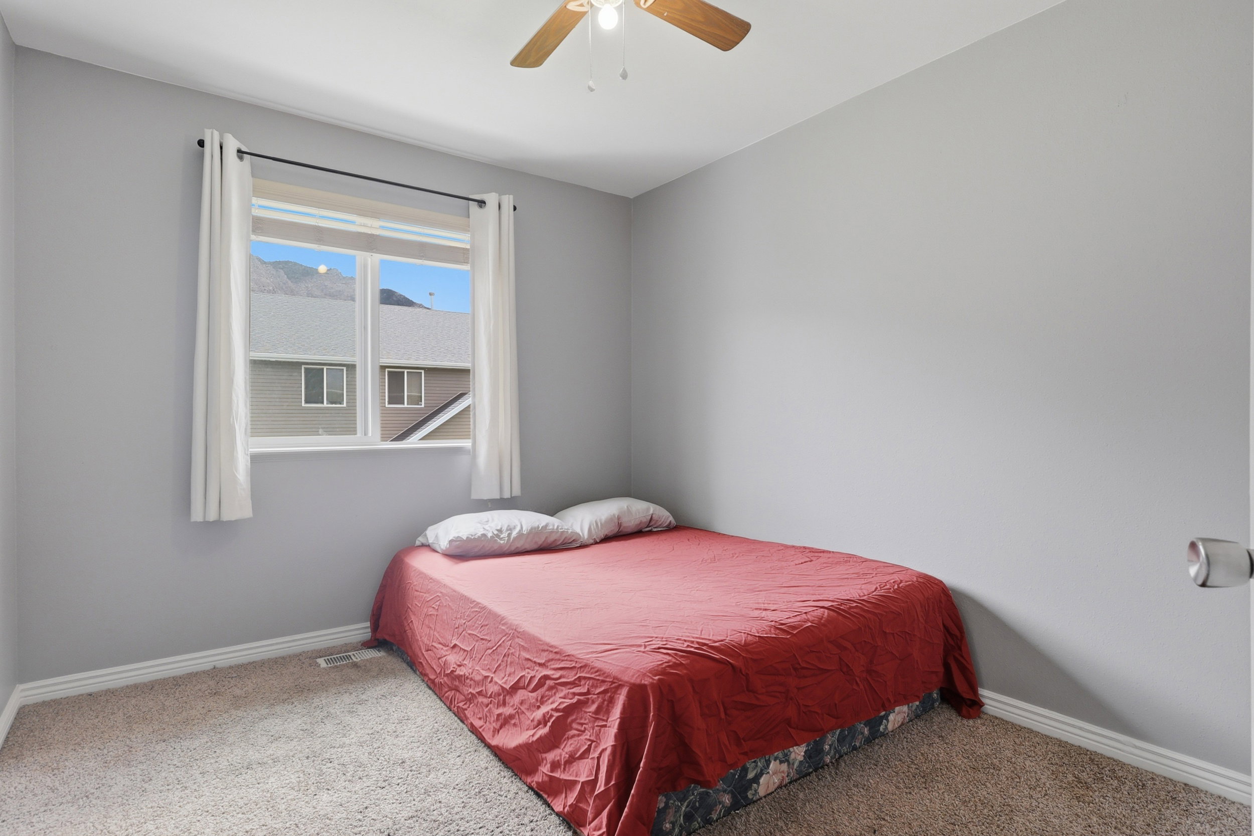 Carpeted room with a ceiling fan, baseboard trim, and a window with a mountain backdrop