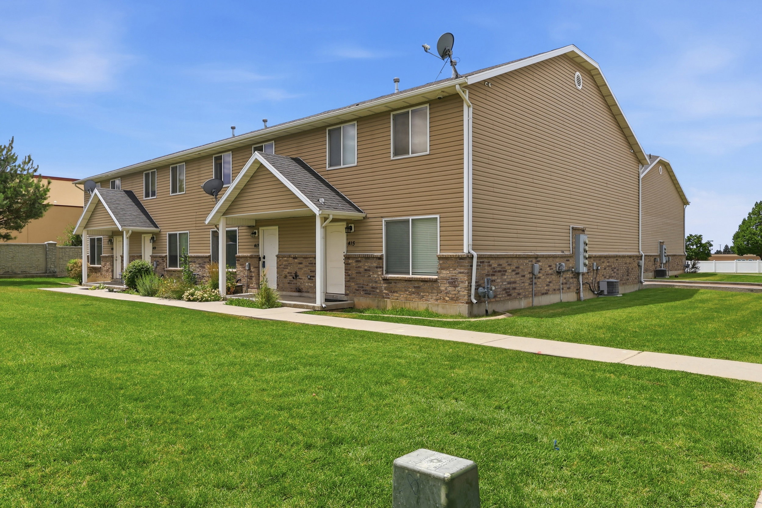 Exterior view of a multi-unit residential building featuring tan siding and a brick facade