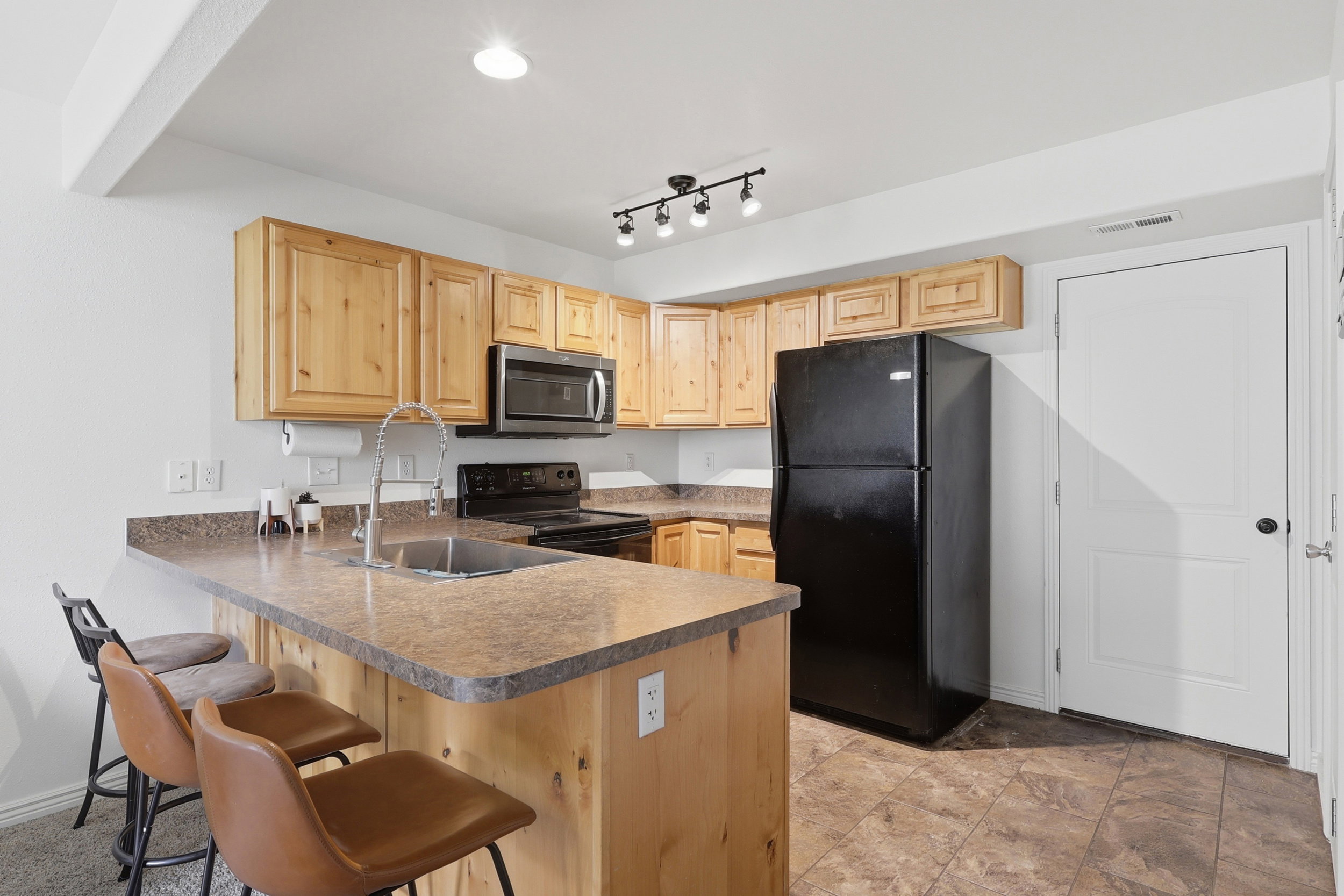 Kitchen featuring wood cabinetry, laminate countertops, a stainless steel microwave, black electric range, and black refrigerator