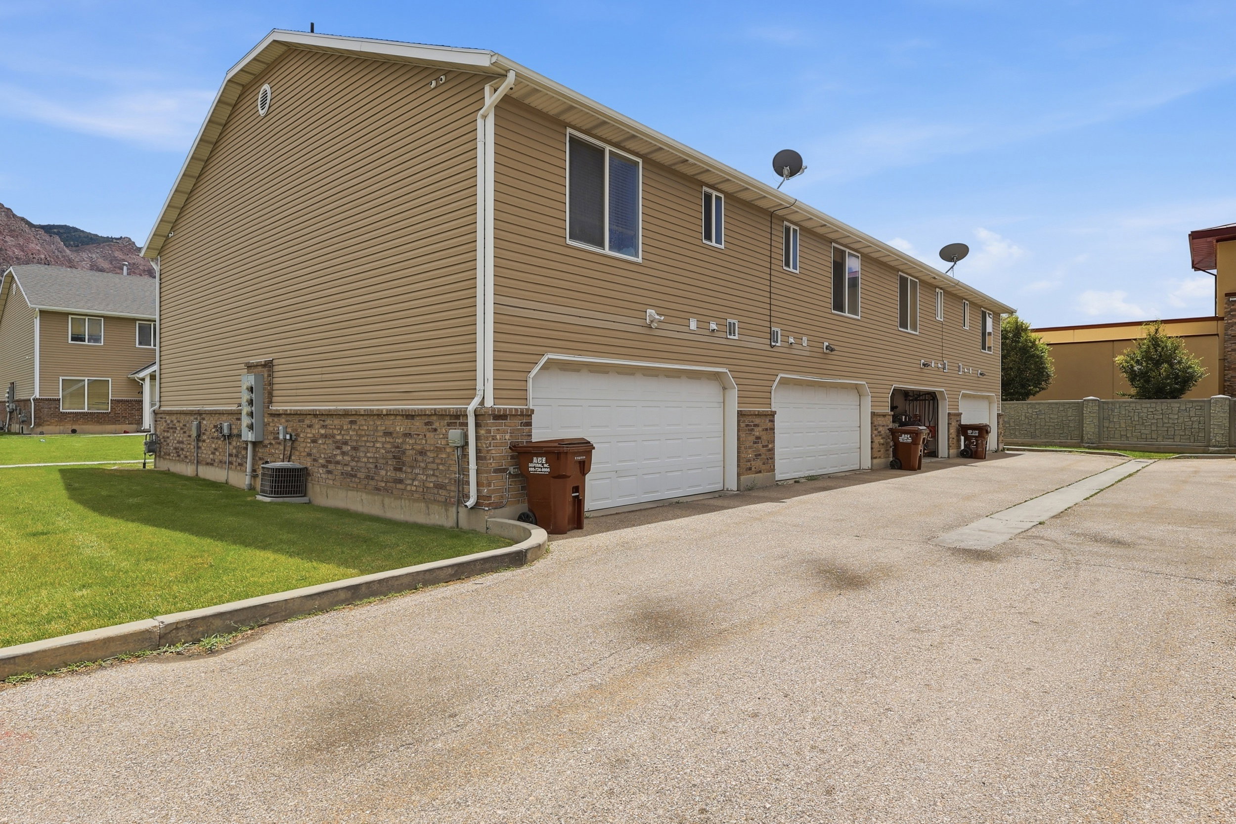 Building exterior featuring tan siding with brick veneer accents, multiple white garage doors, and a paved driveway