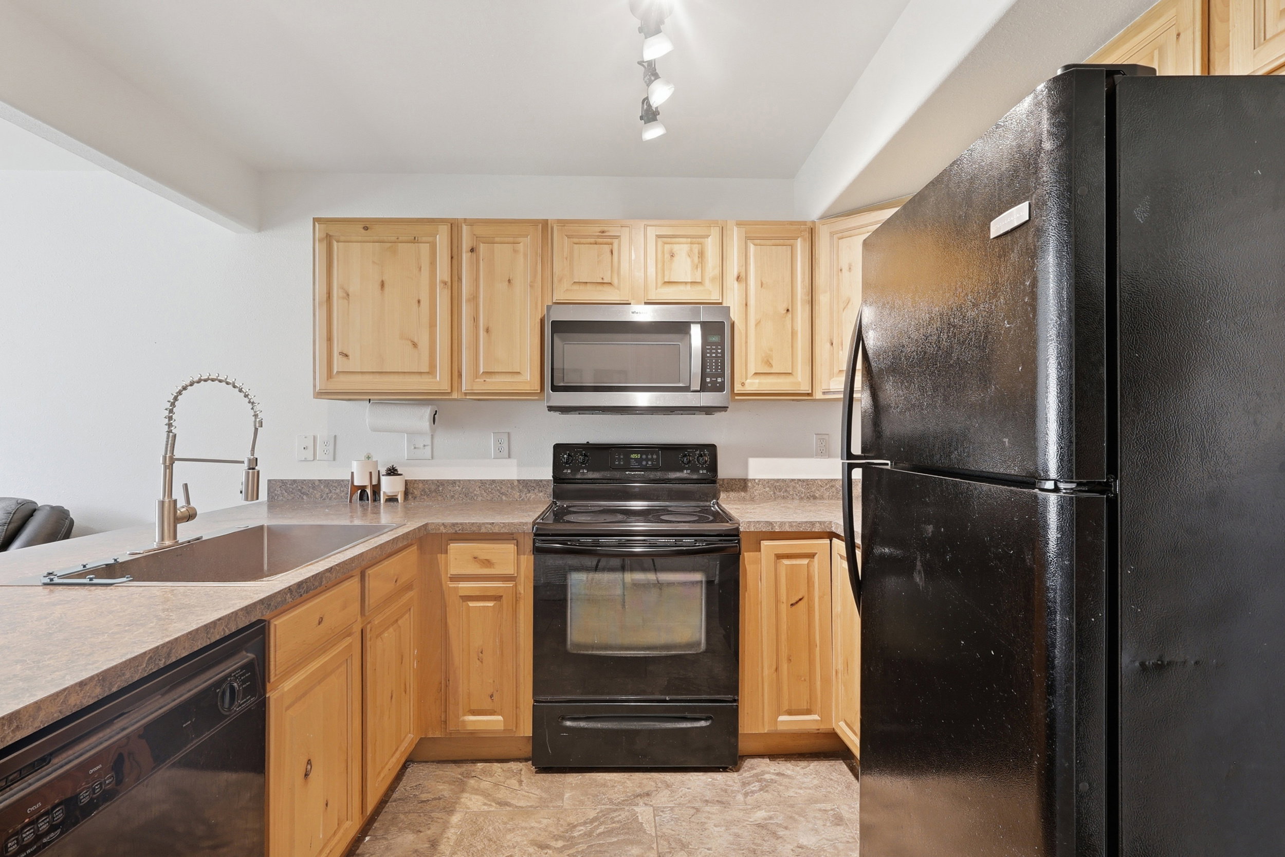 Kitchen featuring light wood cabinetry, laminate countertops, stainless steel microwave, black electric range, and black refrigerator