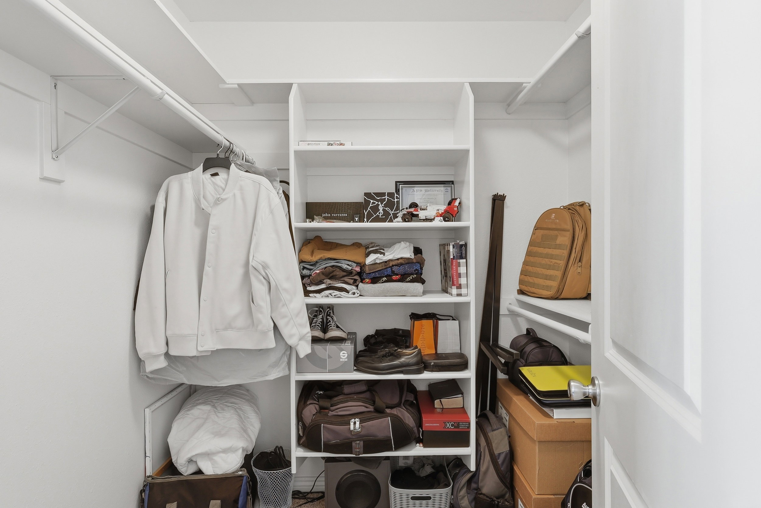 Walk-in closet featuring white built-in shelving, hanging rods, and a white interior door