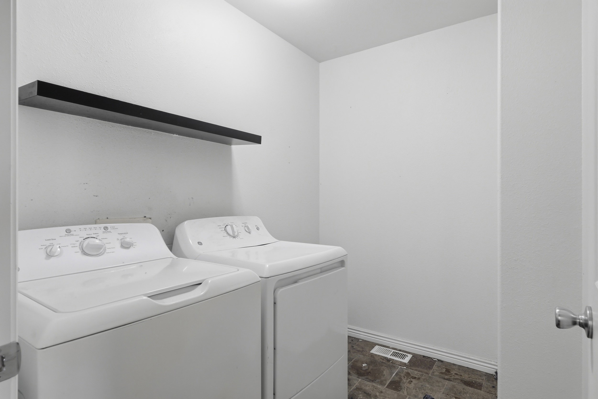 Dedicated laundry area featuring a dark floating shelf and durable tile flooring