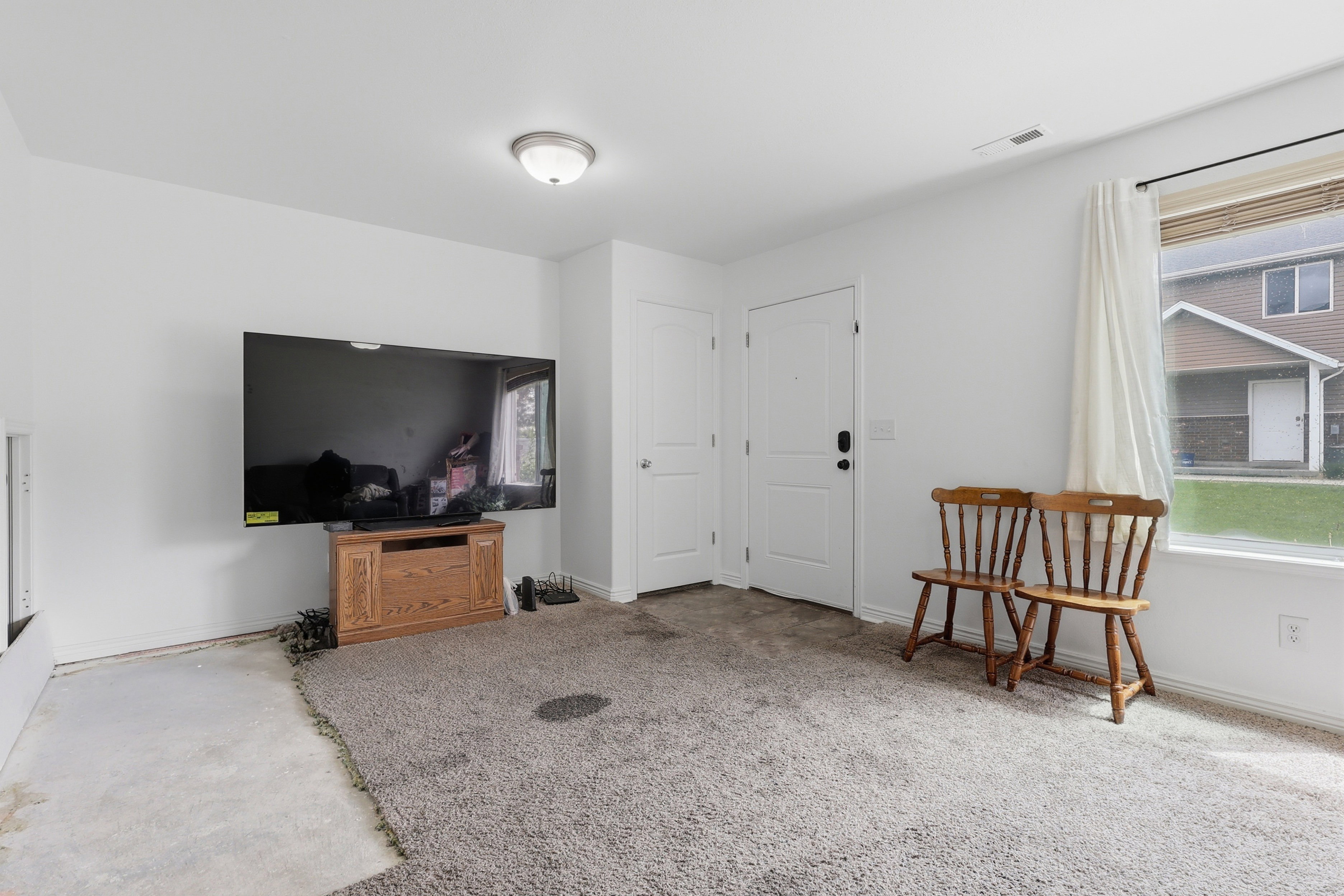Spacious room featuring neutral painted walls, two white doors, an overhead flush-mount light fixture, and a window with white trim