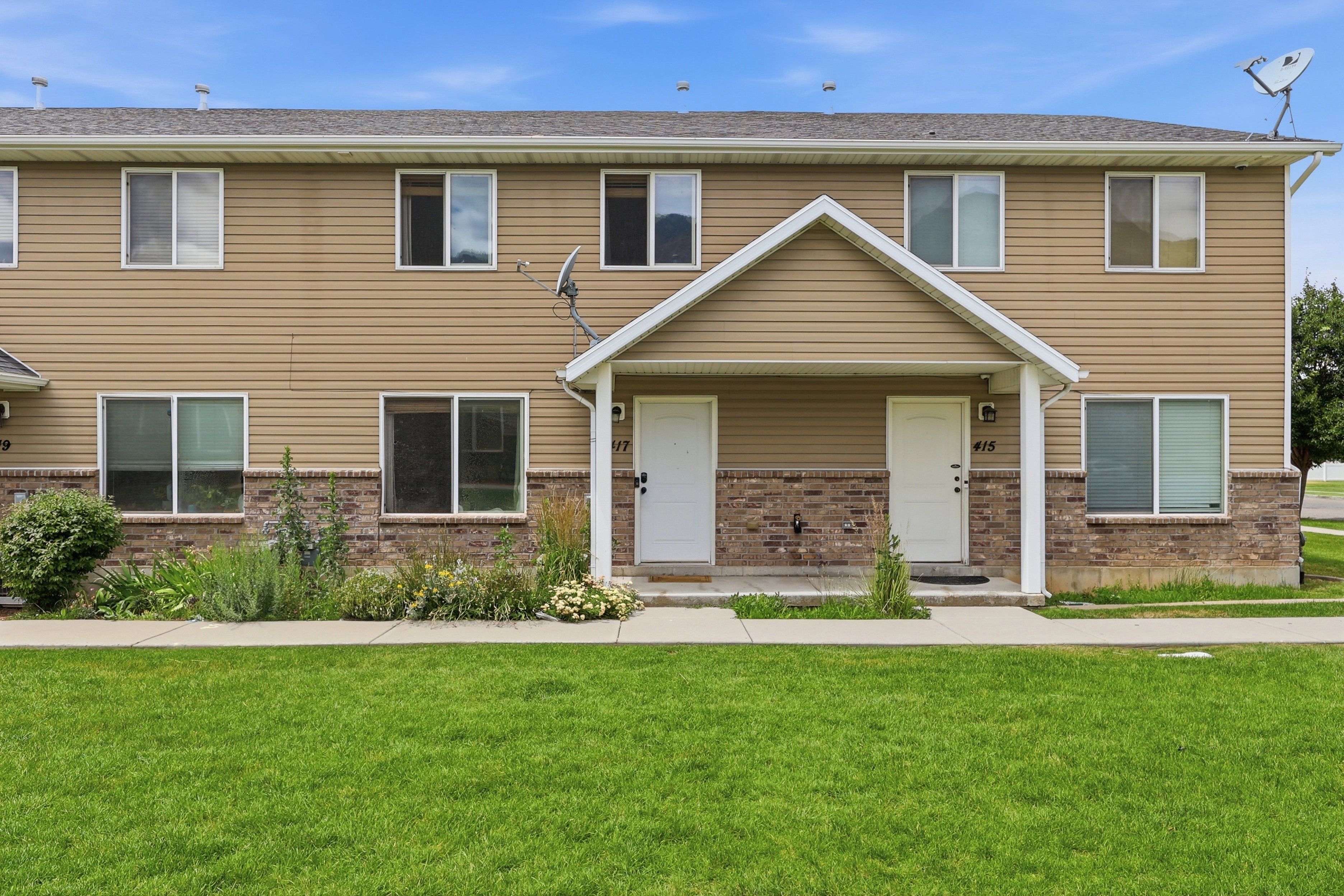 Two-story townhome featuring a neutral siding facade with a brick accent foundation and a covered porch entry