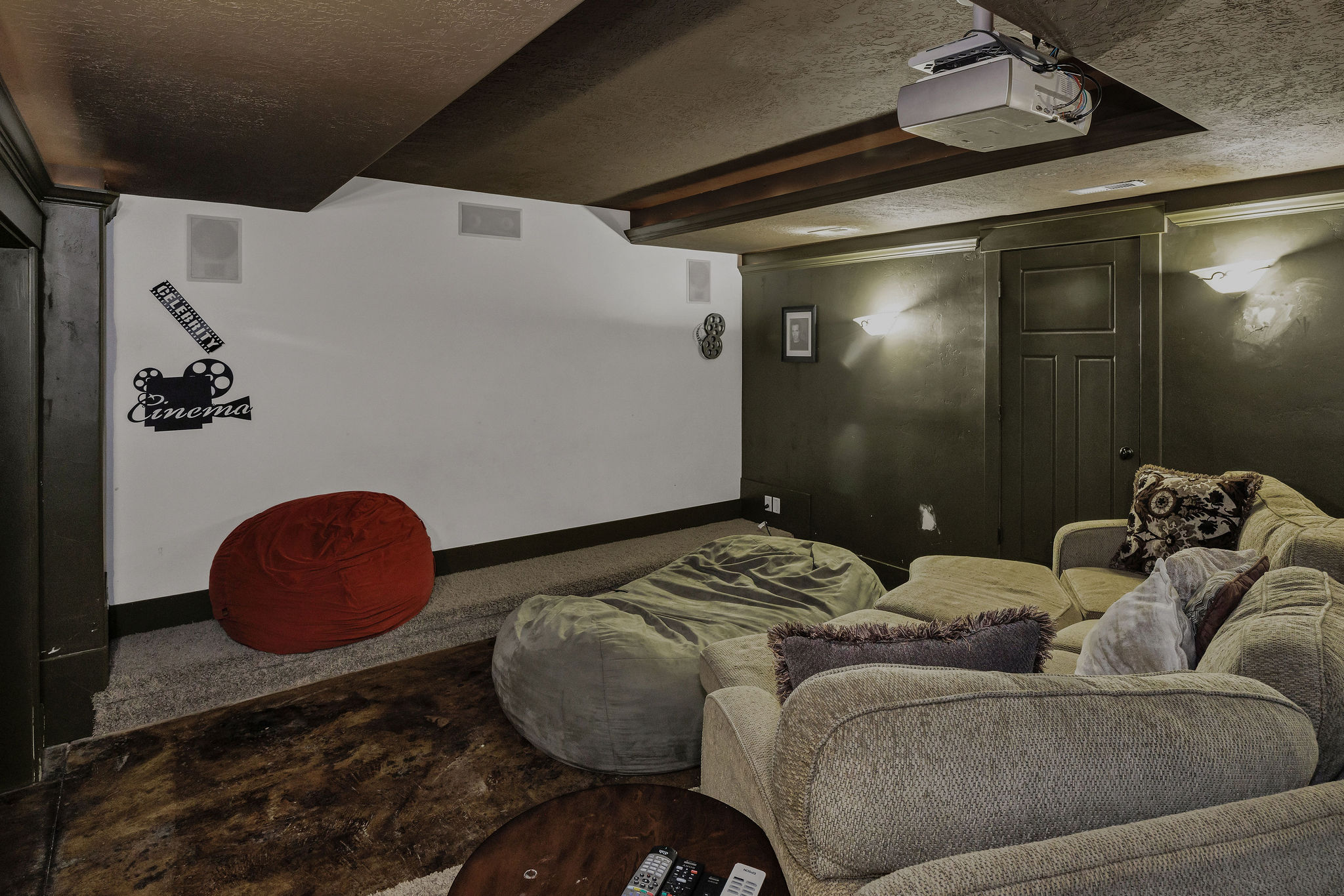 Dedicated media room with a ceiling-mounted projector, built-in ceiling speakers, recessed wall lighting, and a dark accent wall