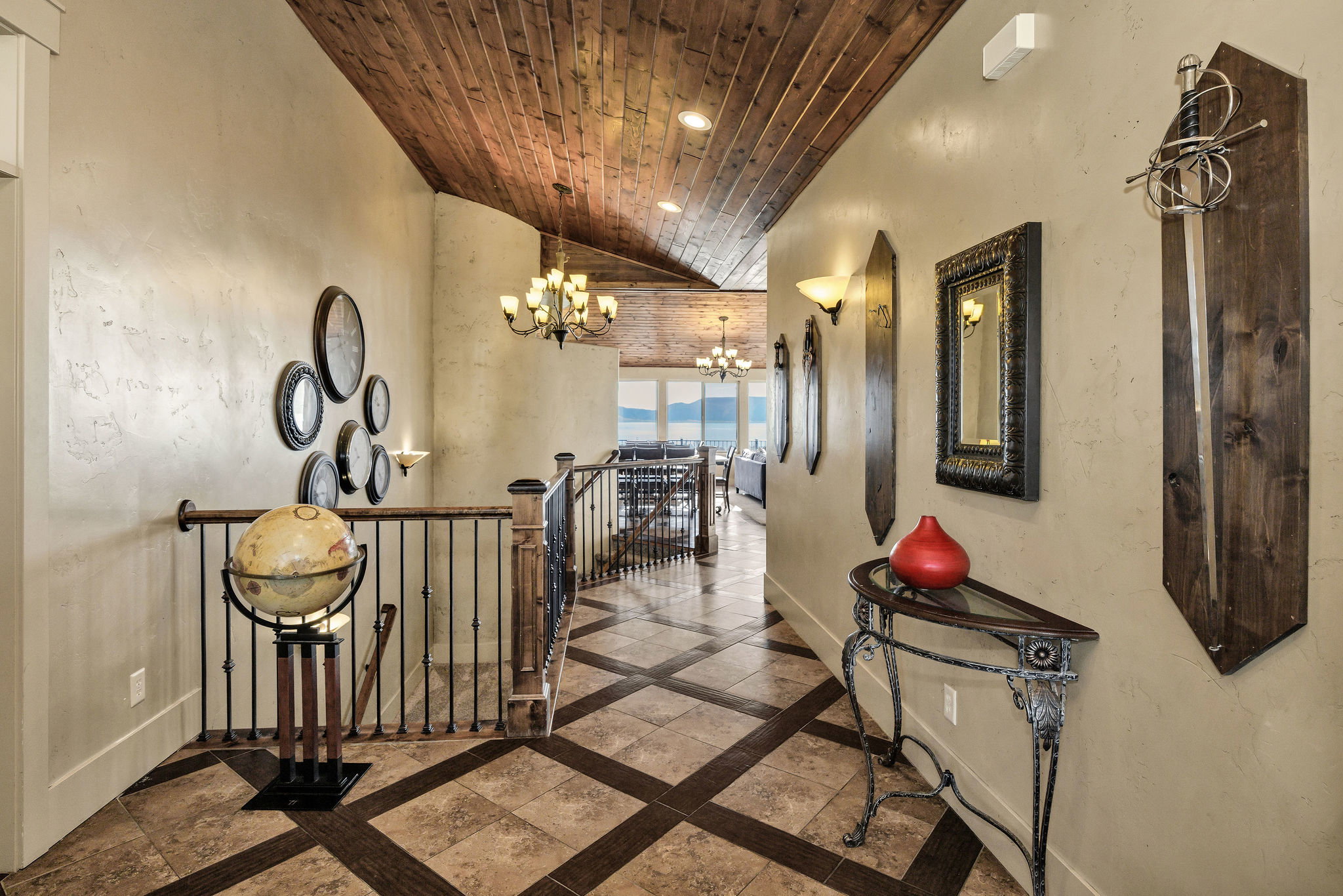 Hallway featuring wood-finish ceiling, patterned tile flooring, wrought iron railings, and sconce lighting