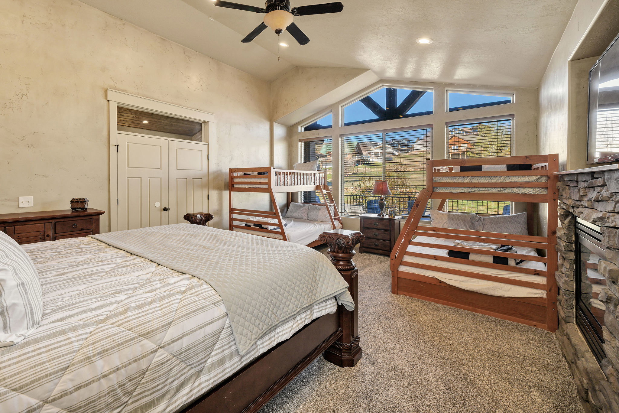 Bedroom featuring vaulted ceilings, a stone-faced fireplace, and expansive windows