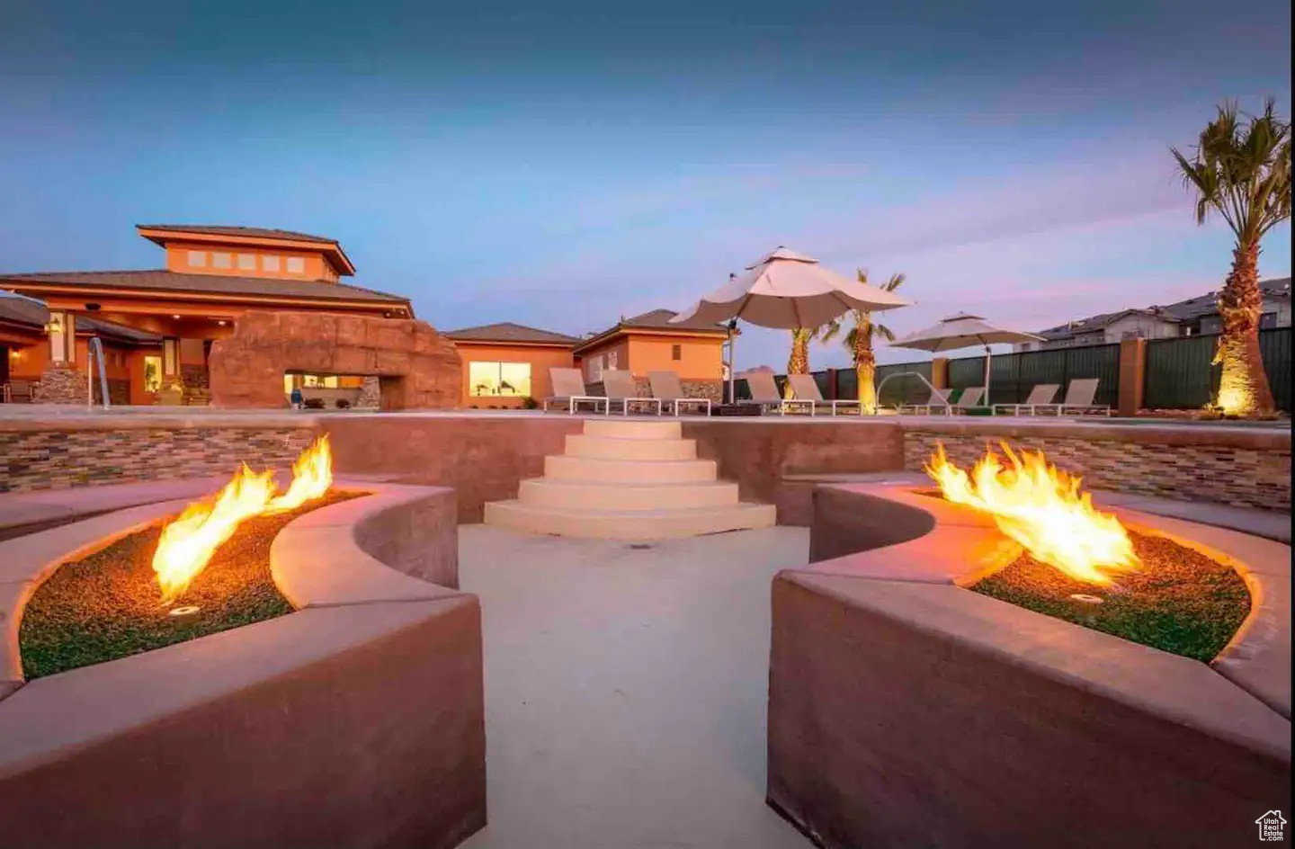 Expansive outdoor space featuring dual built-in fire pits, terraced concrete steps, a multi-level patio, stacked stone accents, and stucco exterior finishes