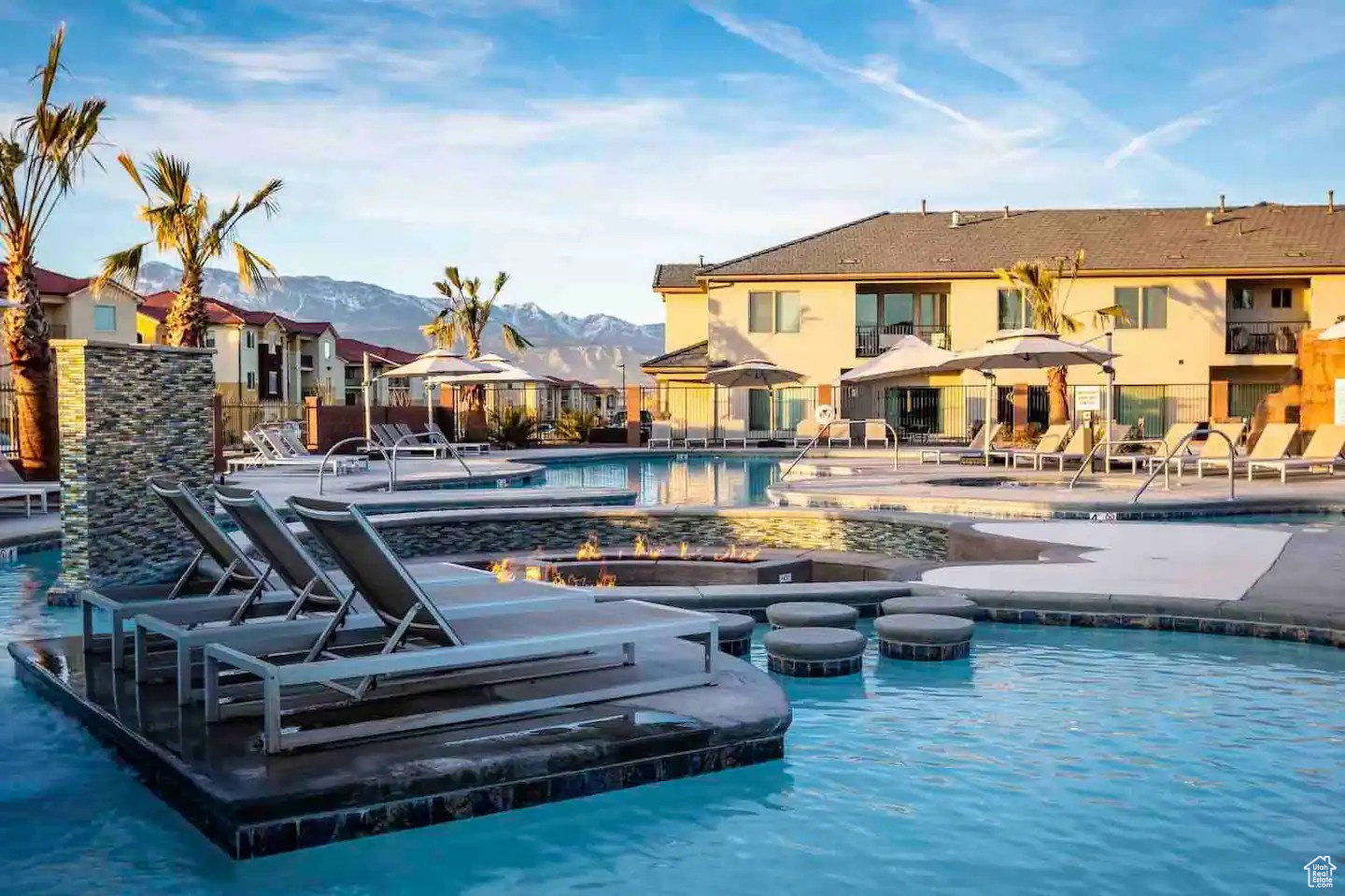 Resort-style aquatic amenity featuring a large swimming pool, integrated fire pits, in-pool lounge seating, and surrounding sun loungers