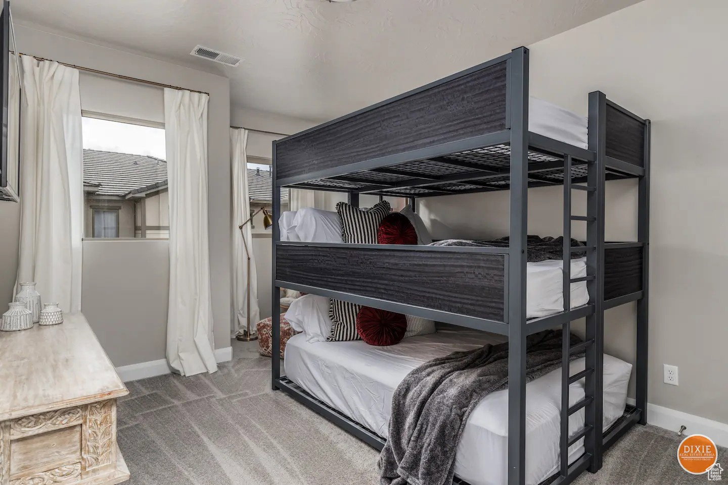 Room featuring a three-tier bunk bed with a dark metal frame and wood-look panels, light gray carpeting, and neutral-toned walls