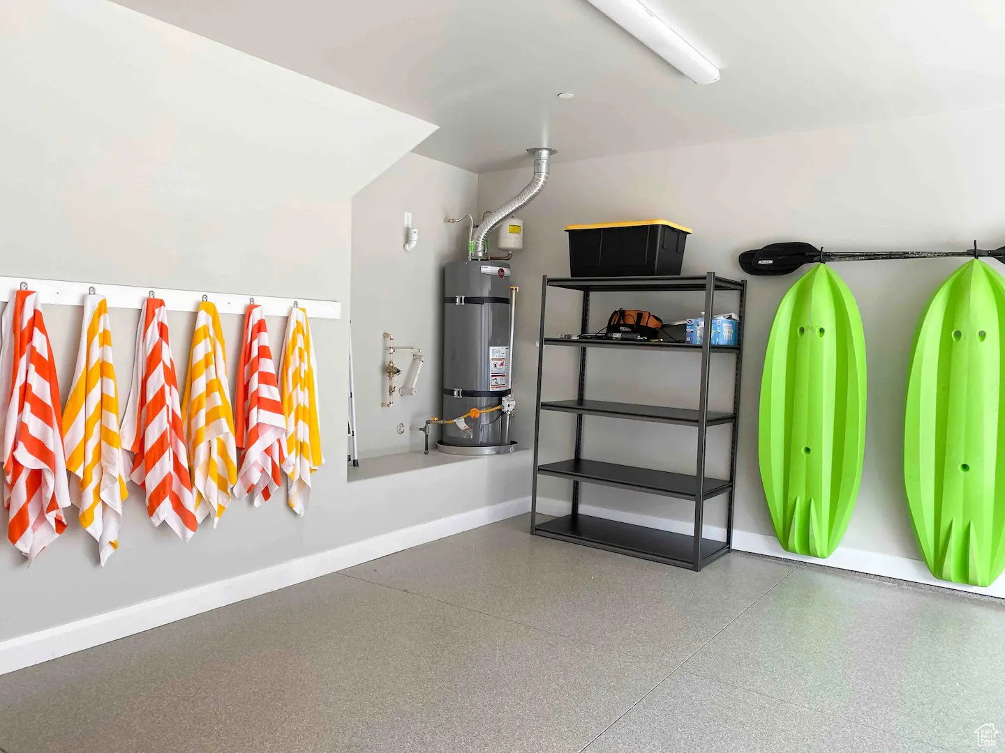 Garage space featuring speckled epoxy flooring, a wall-mounted water heater, a built-in shelving unit, overhead fluorescent lighting, and a wall-mounted rack system