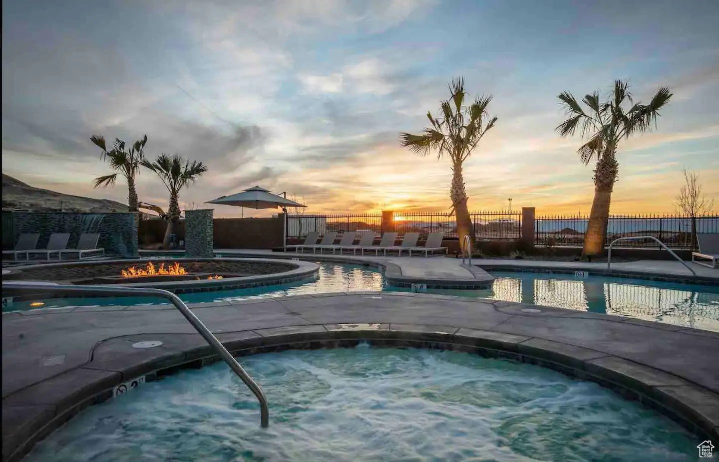 Expansive pool area featuring a large spa with a stainless steel handrail, a fire pit, and multiple lounge chairs
