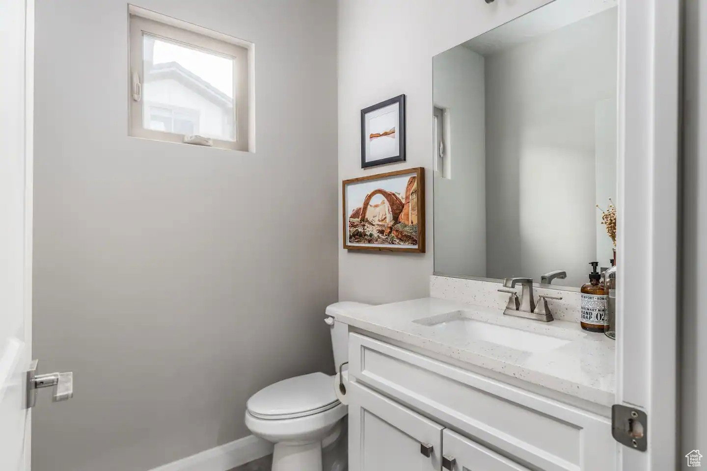 Powder room featuring a white single-sink vanity with a speckled countertop, a large wall-mounted mirror, a modern toilet, and a high-set window