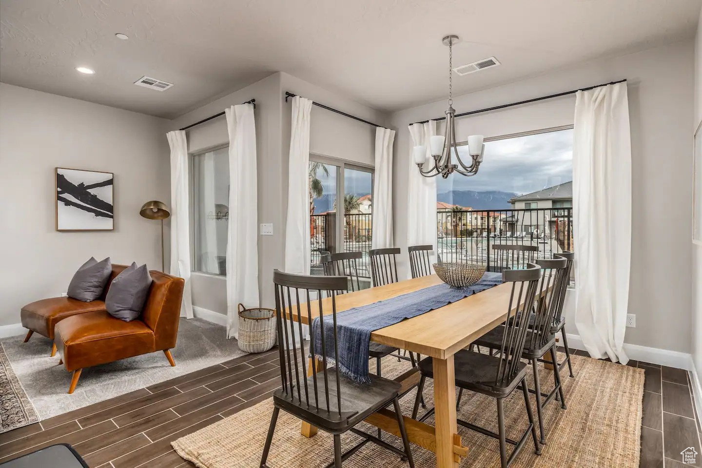 Spacious dining area featuring wood-finish flooring, a contemporary chandelier, large windows with a mountain backdrop, and light-toned wall paint