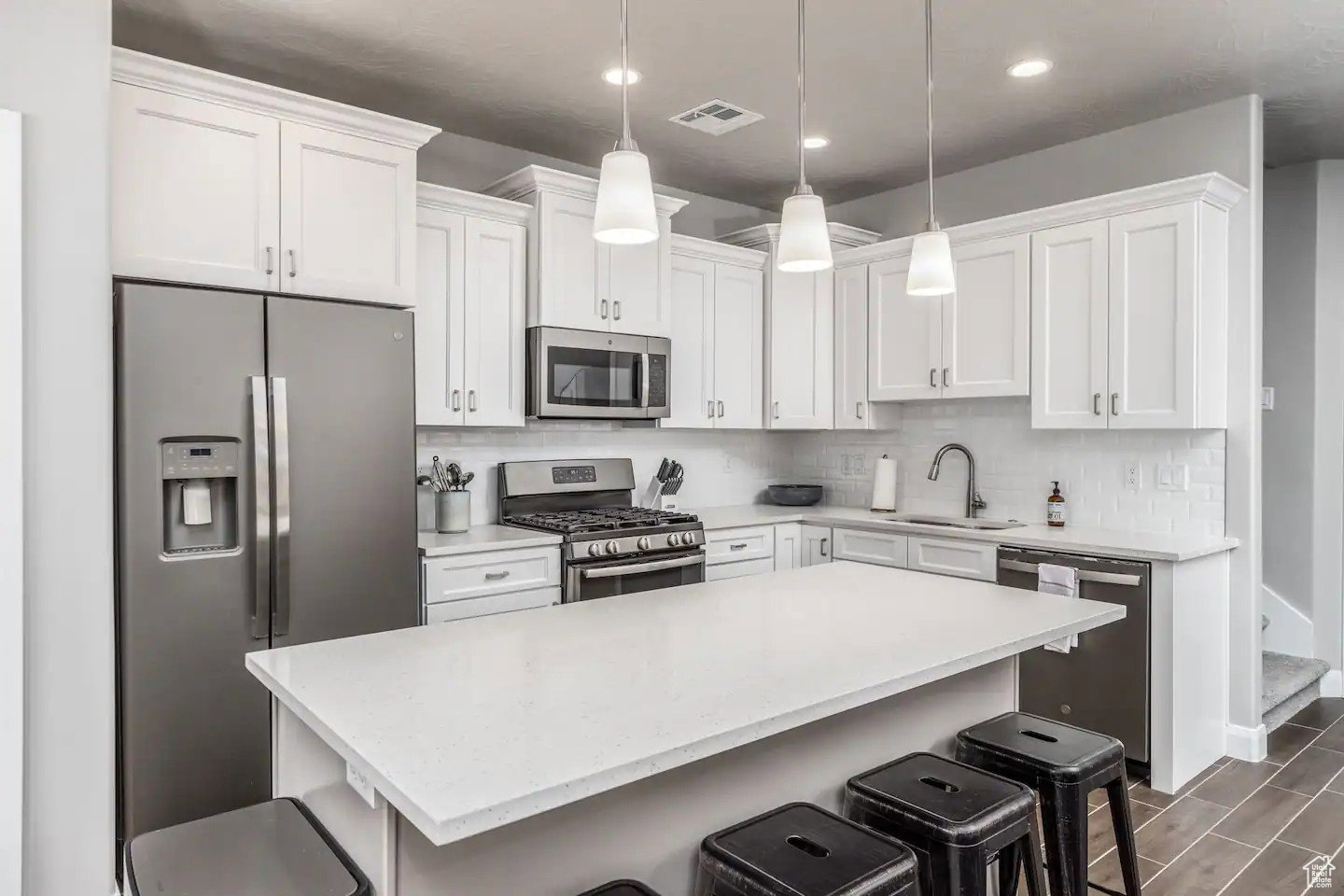 Modern kitchen featuring a central island with countertop seating, white shaker cabinetry, stainless steel appliances, and a subway tile backsplash