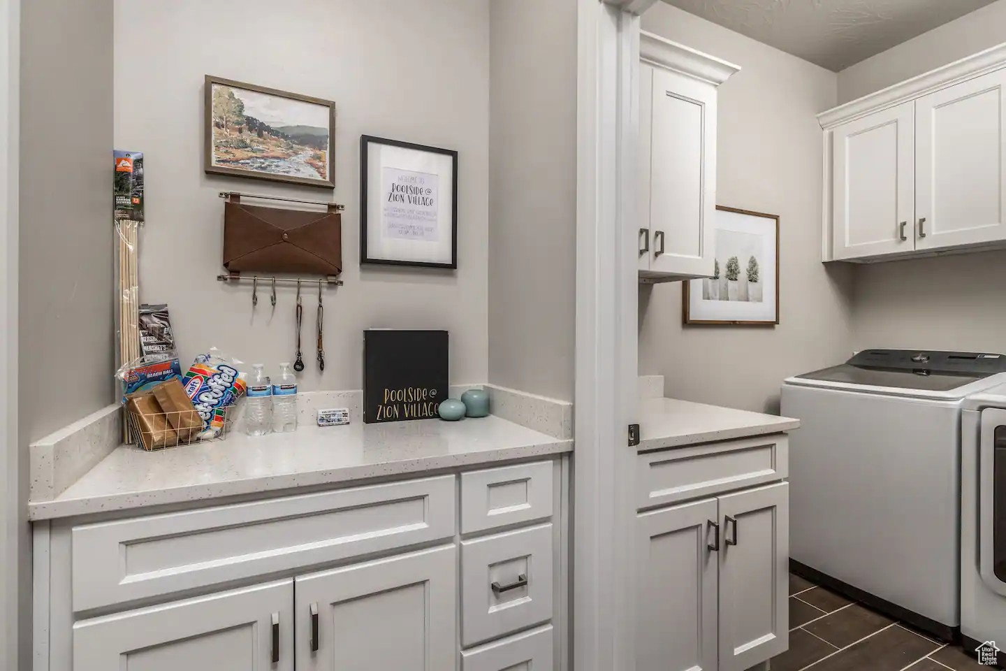 Laundry area featuring white shaker-style cabinetry, light-toned countertops, and dark tile flooring