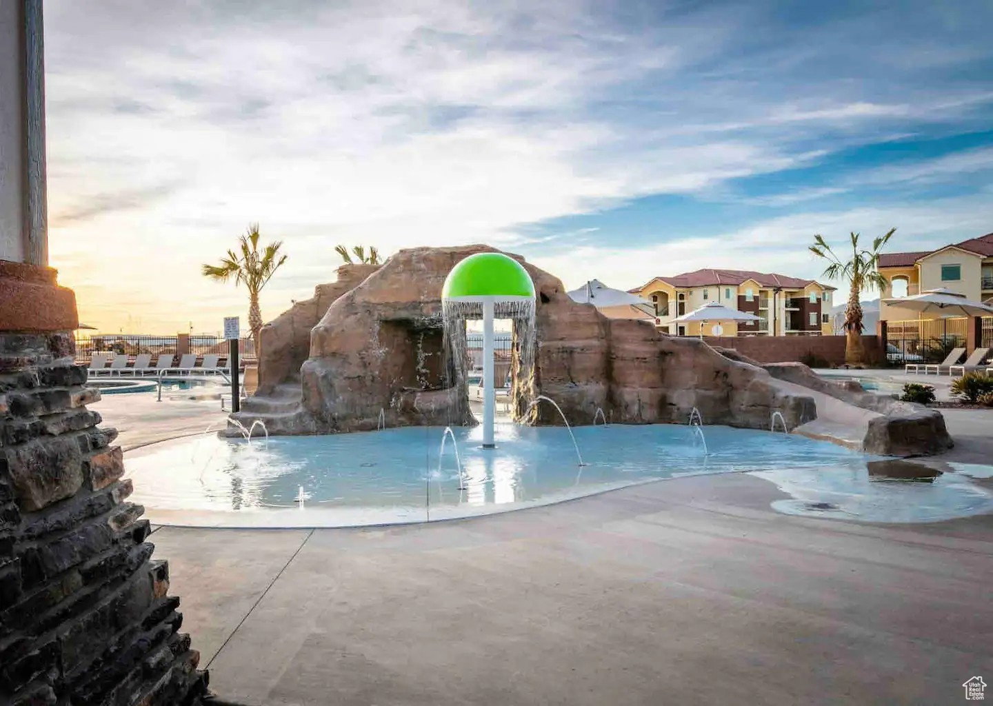 Pool area featuring a rock-formation water slide, splash pad with fountain jets, and a mushroom-shaped water feature