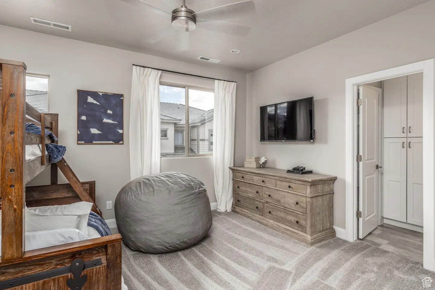 Bedroom featuring a ceiling fan, dual windows with white curtains, patterned carpet flooring, and a built-in closet with white cabinetry