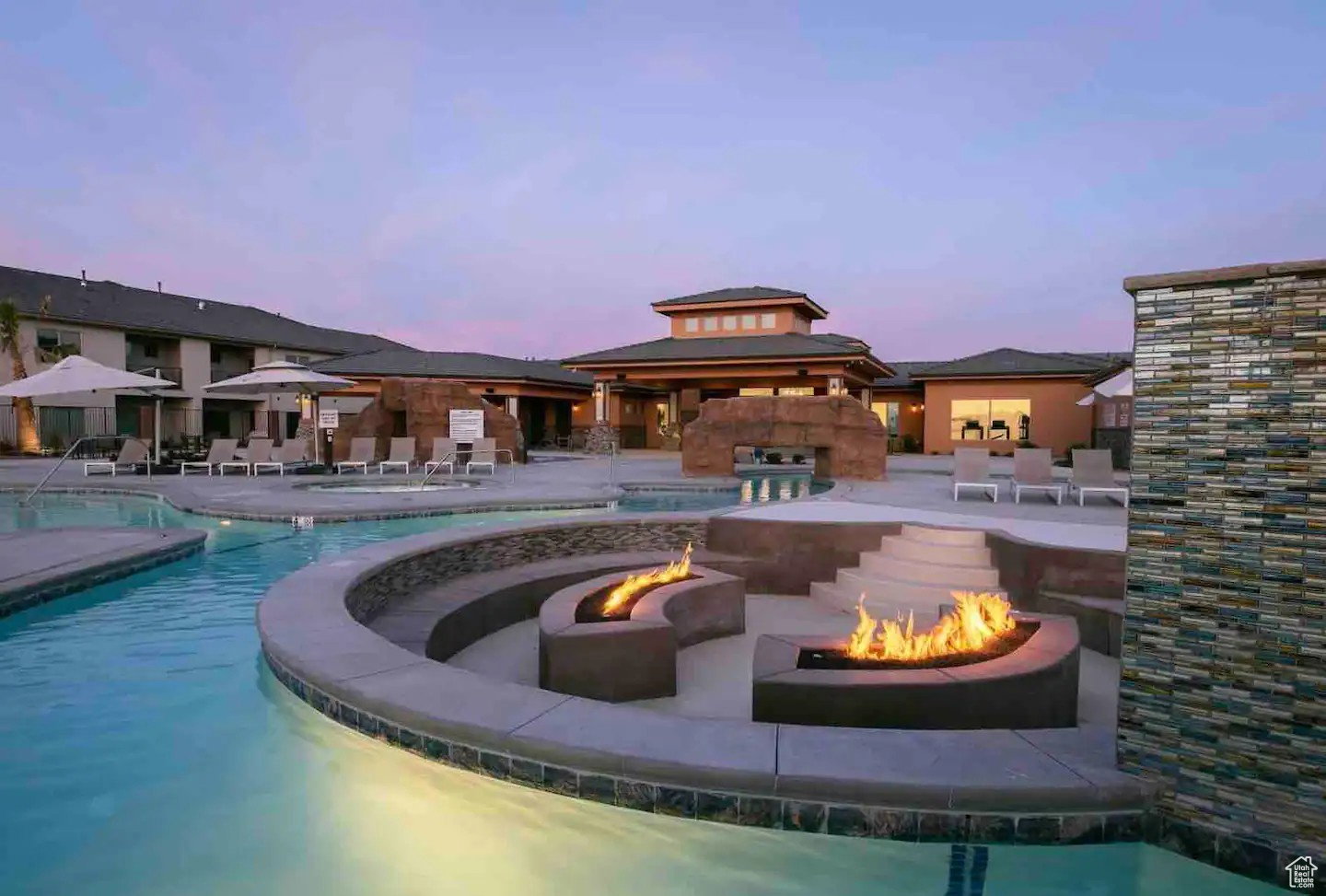 Resort-style pool area featuring multiple fire pits, a stepped concrete seating area, and a flowing water feature