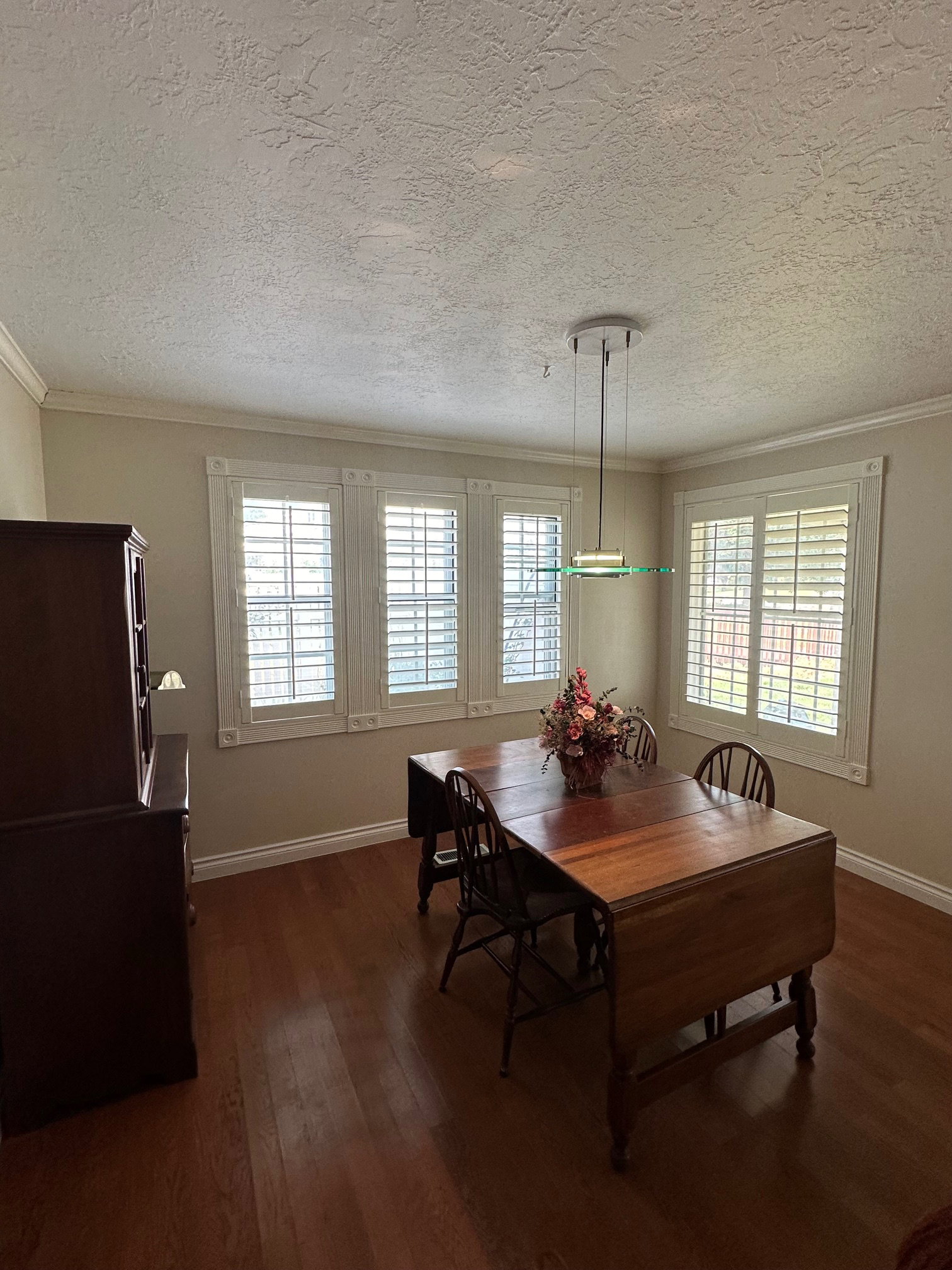 Room featuring wood-finish flooring, crown molding, and a contemporary pendant light fixture