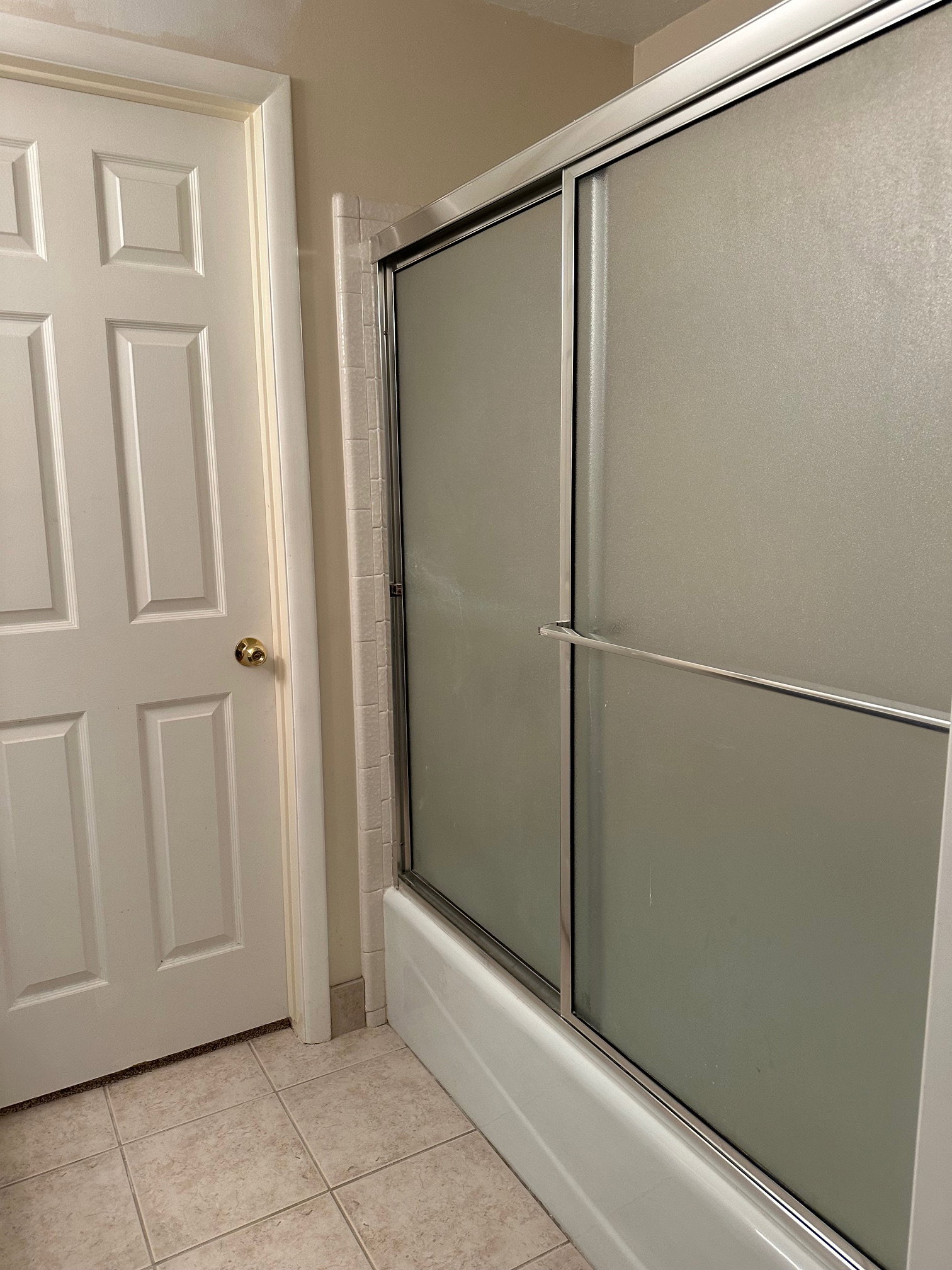 Bathtub with sliding frosted glass enclosure and chrome framing in the Primary bathroom.