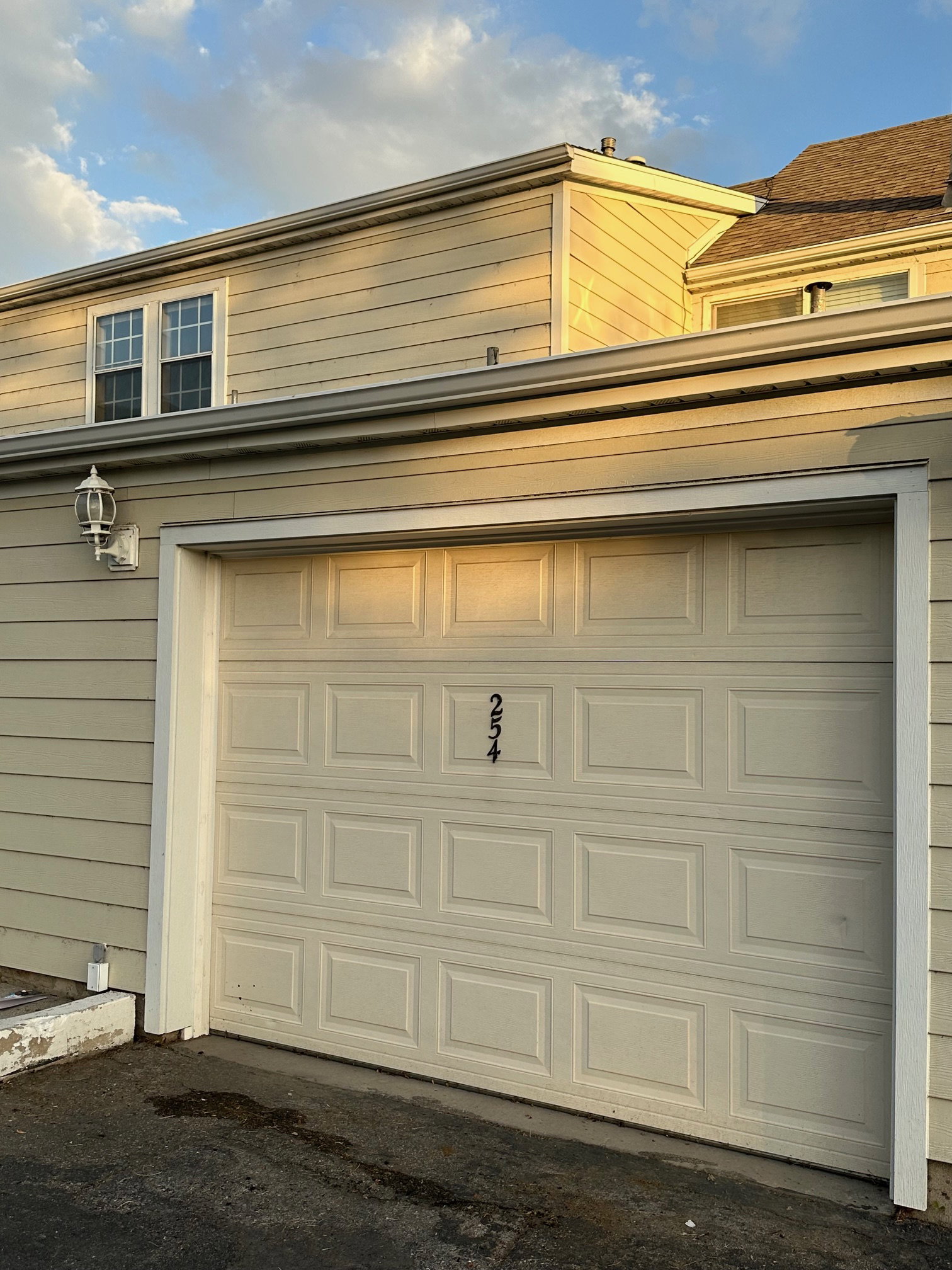Attached garage with panel door, exterior wall lantern, house numbers, and light-colored siding