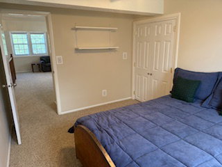 Carpeted room with a bi-fold door closet, wall-mounted shelving, and a doorway opening to upstairs family room.