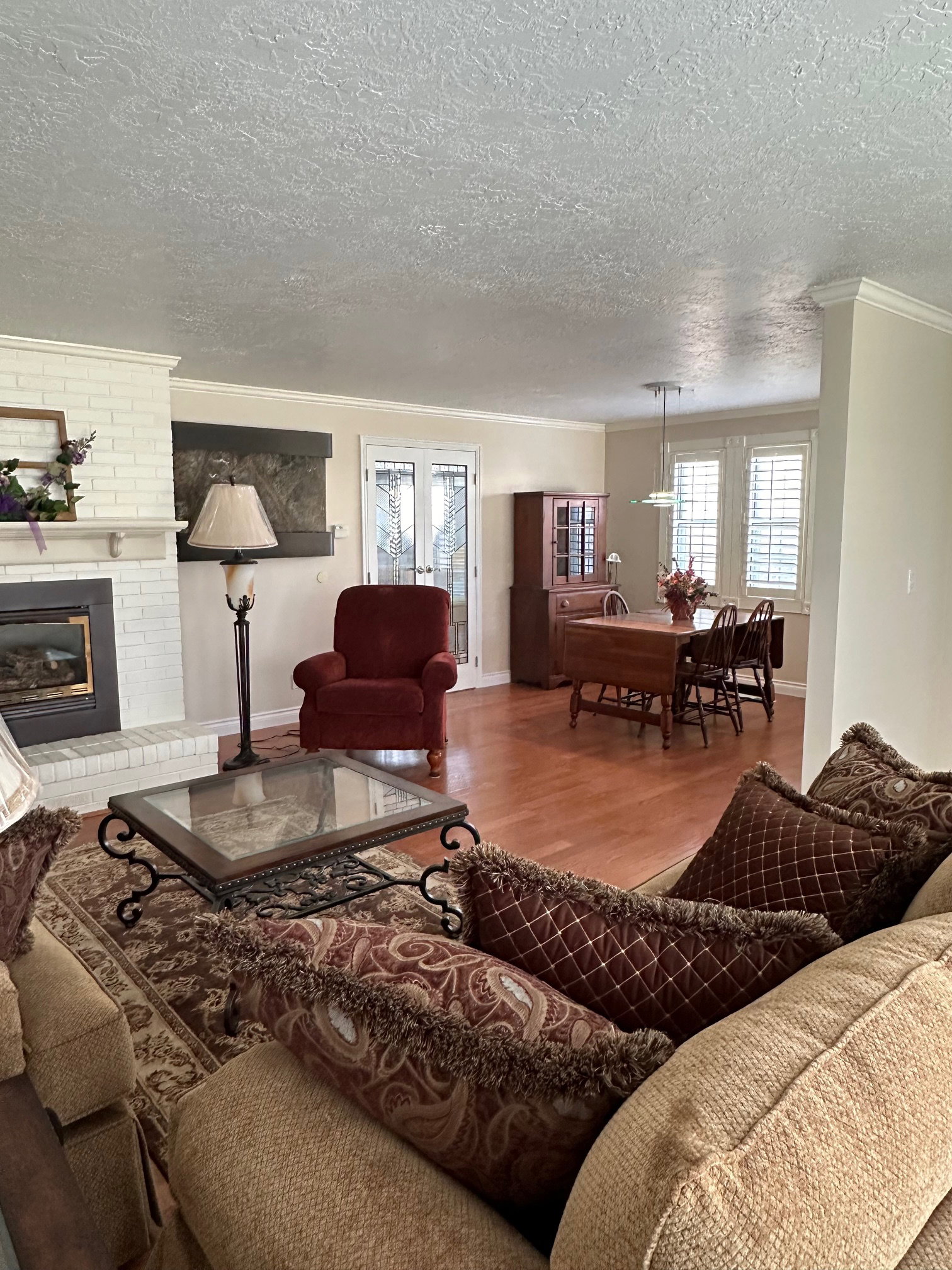 Open-concept living area featuring wood-finish flooring, a white brick fireplace, and crown molding