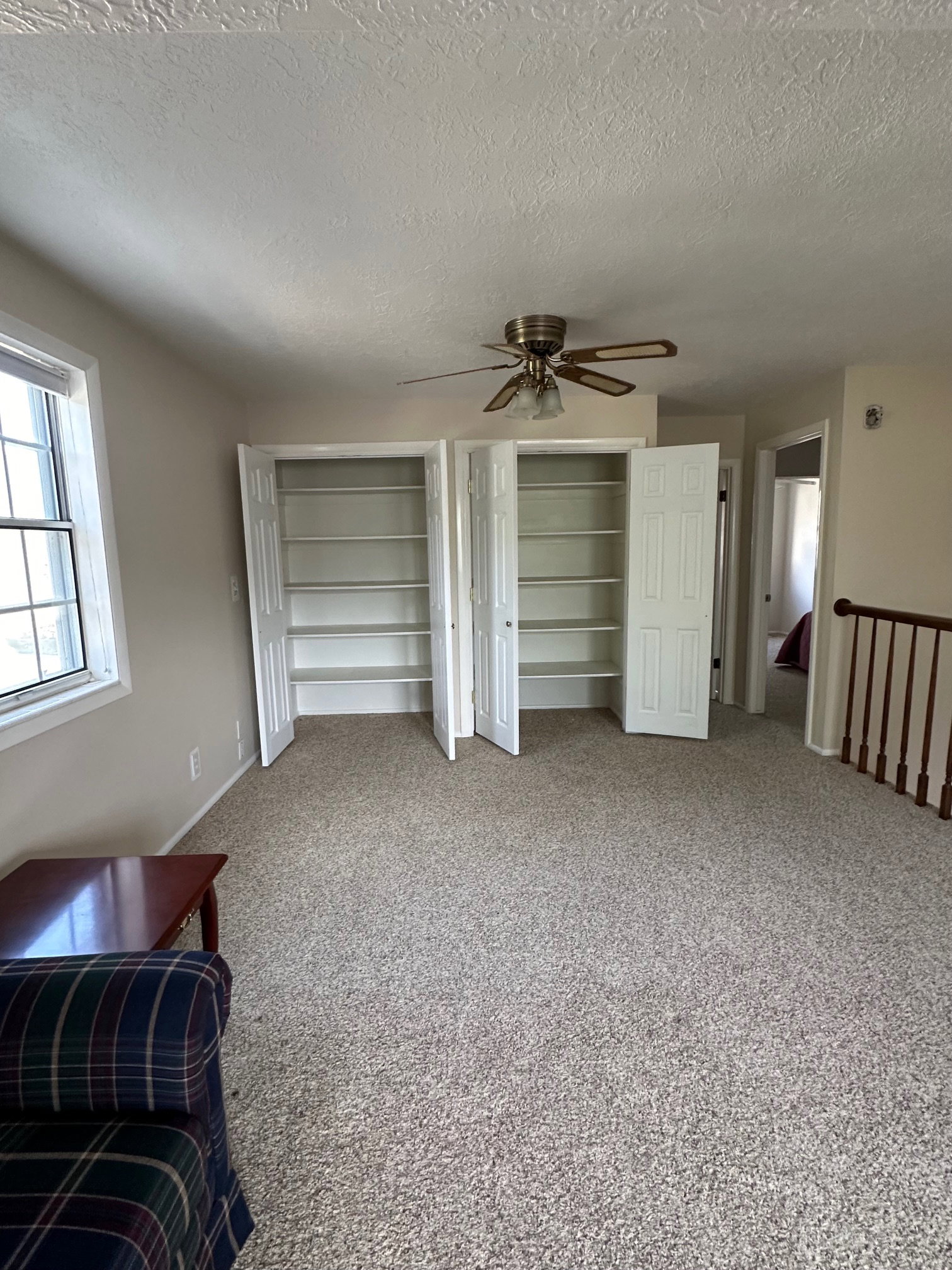 Carpeted interior space featuring two built-in storage closets with bi-fold doors, a ceiling fan, and a window in the second floor family room.