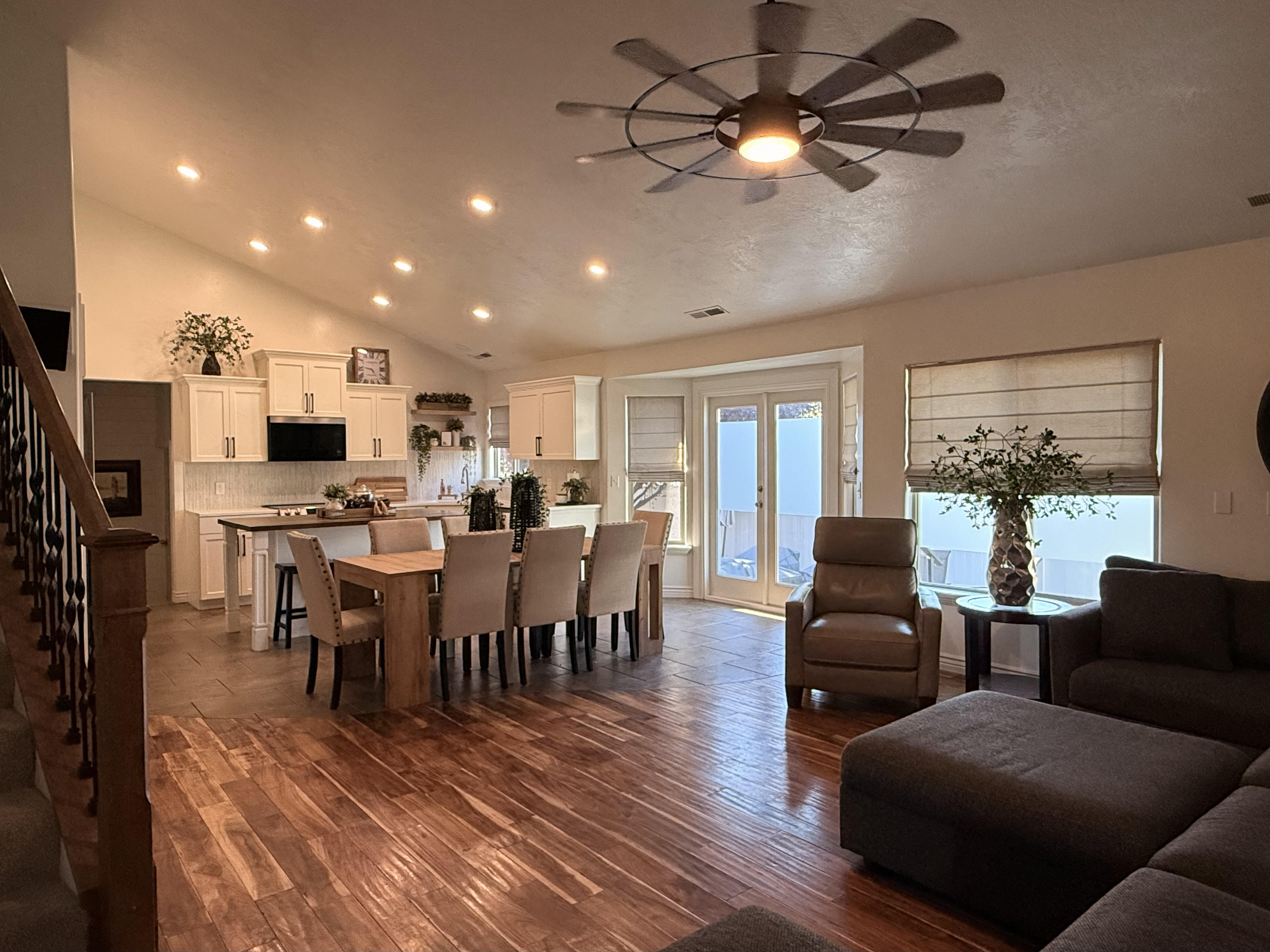 Open-concept living area featuring a vaulted ceiling with recessed lighting, wood-finish flooring, a kitchen with white cabinetry and an island, French patio doors, and a ceiling fan with a metallic finish
