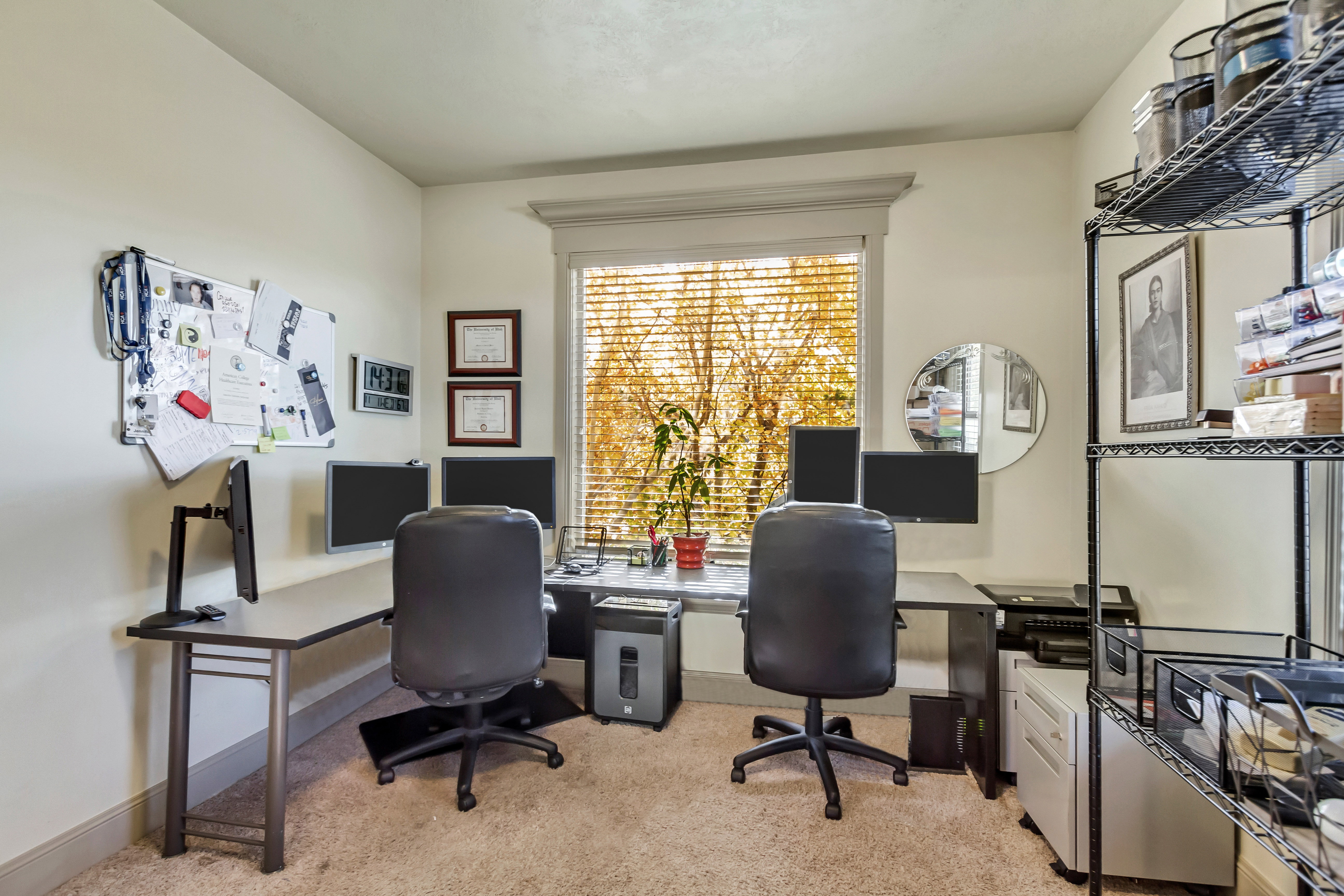 Dedicated office space featuring a large window with horizontal blinds, neutral wall paint, and a built-in metal shelving unit