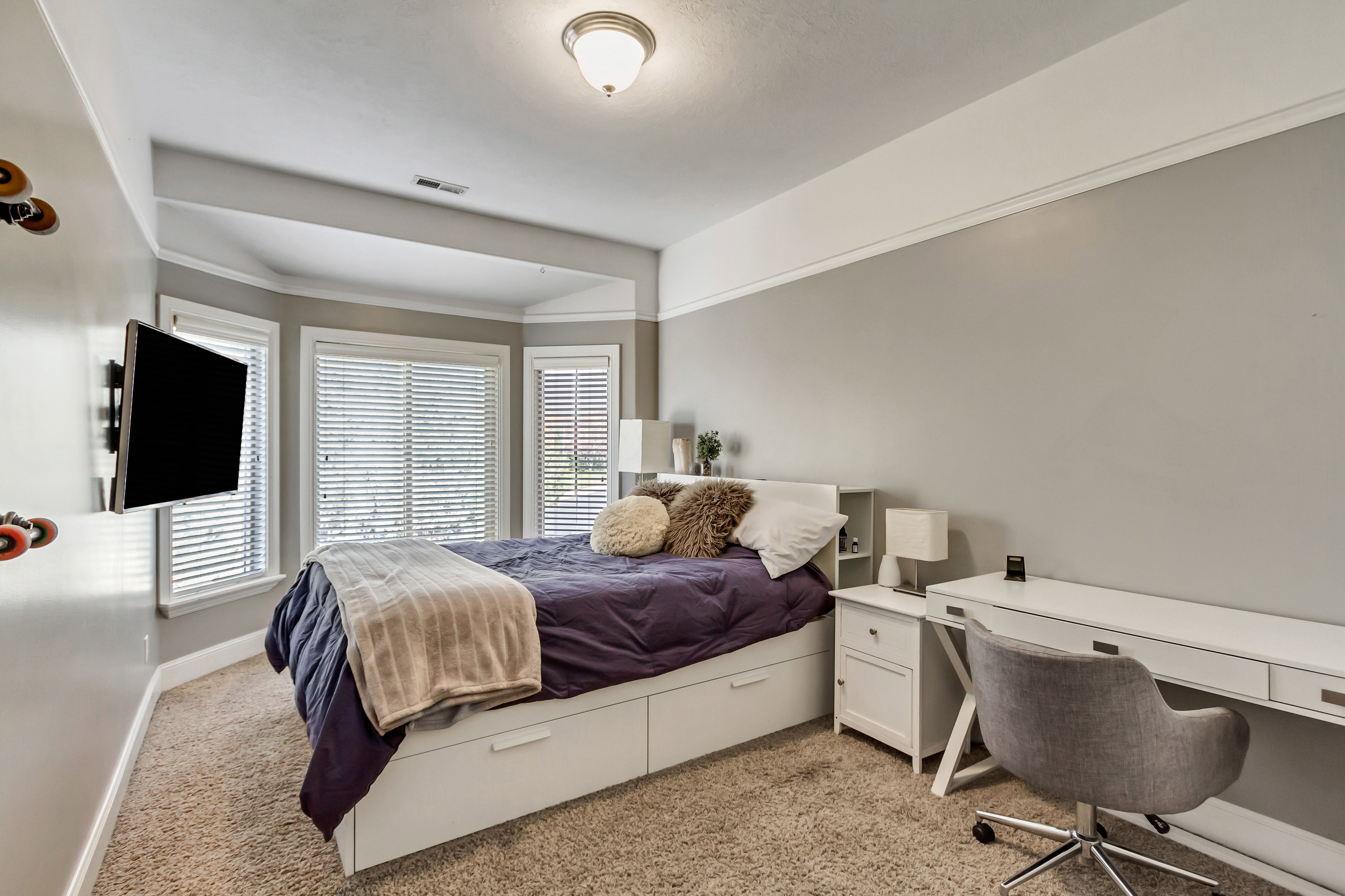 Carpeted room featuring a bay window with blinds, a wall-mounted television, and a built-in desk area