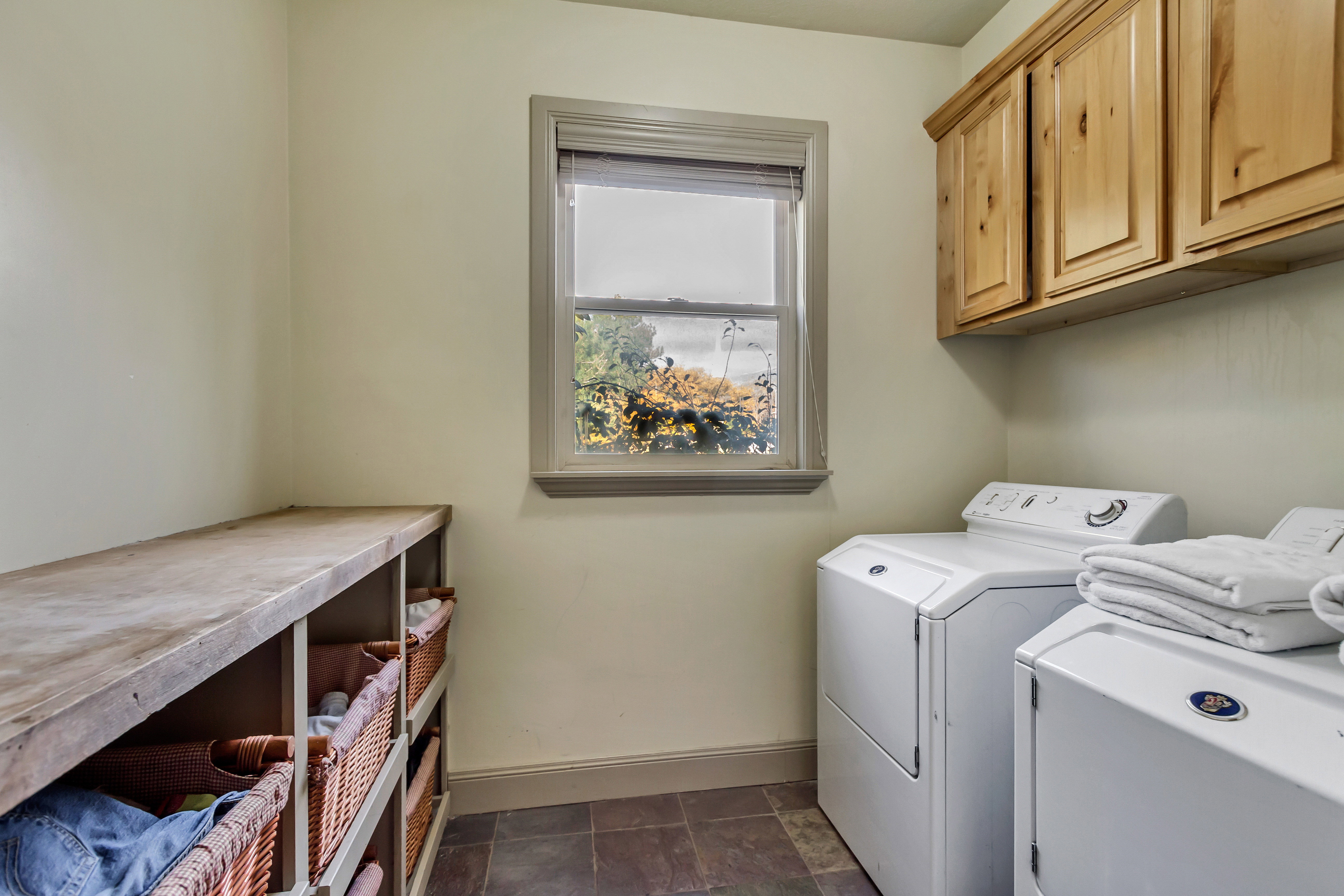 Dedicated utility space featuring natural wood-finish cabinetry, an expansive wood-finish countertop with integrated shelving, and durable slate tile flooring