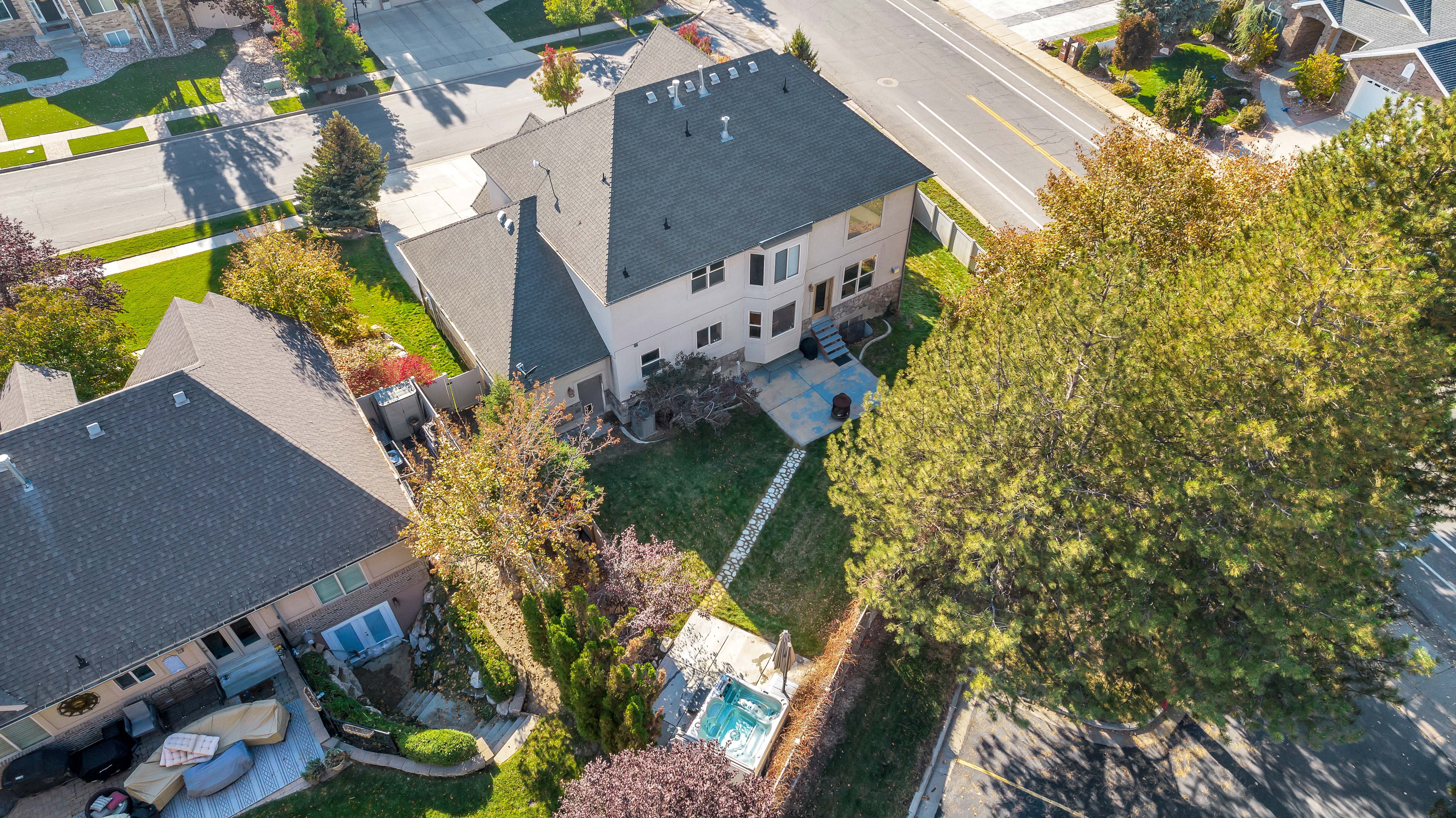 Expansive backyard featuring a manicured lawn, established trees, a paver patio, and an inground spa