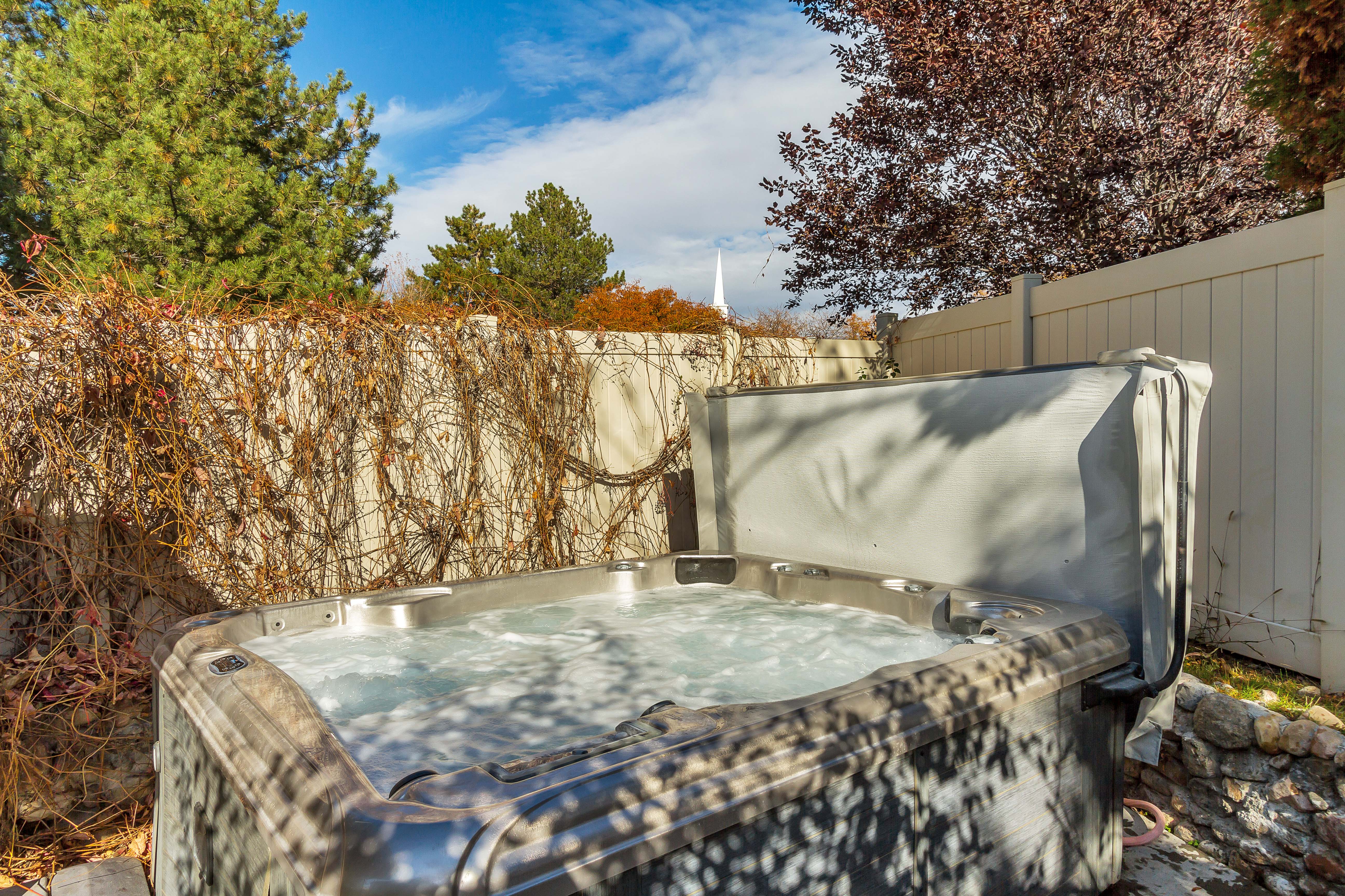 Outdoor spa with partial cover, surrounded by a privacy fence and mature landscaping