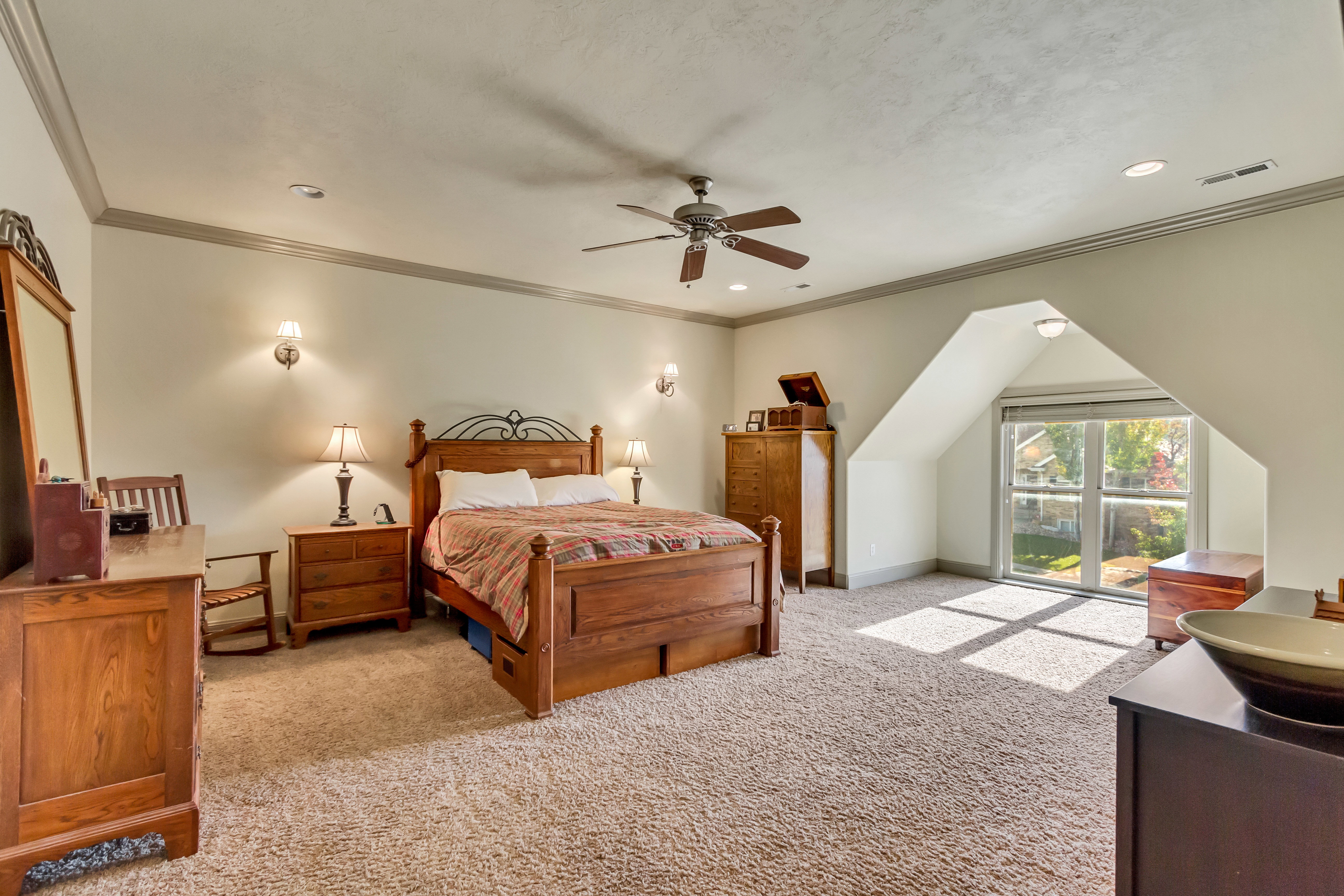 Carpeted bedroom featuring a large window, ceiling fan, recessed lighting, and wall sconces
