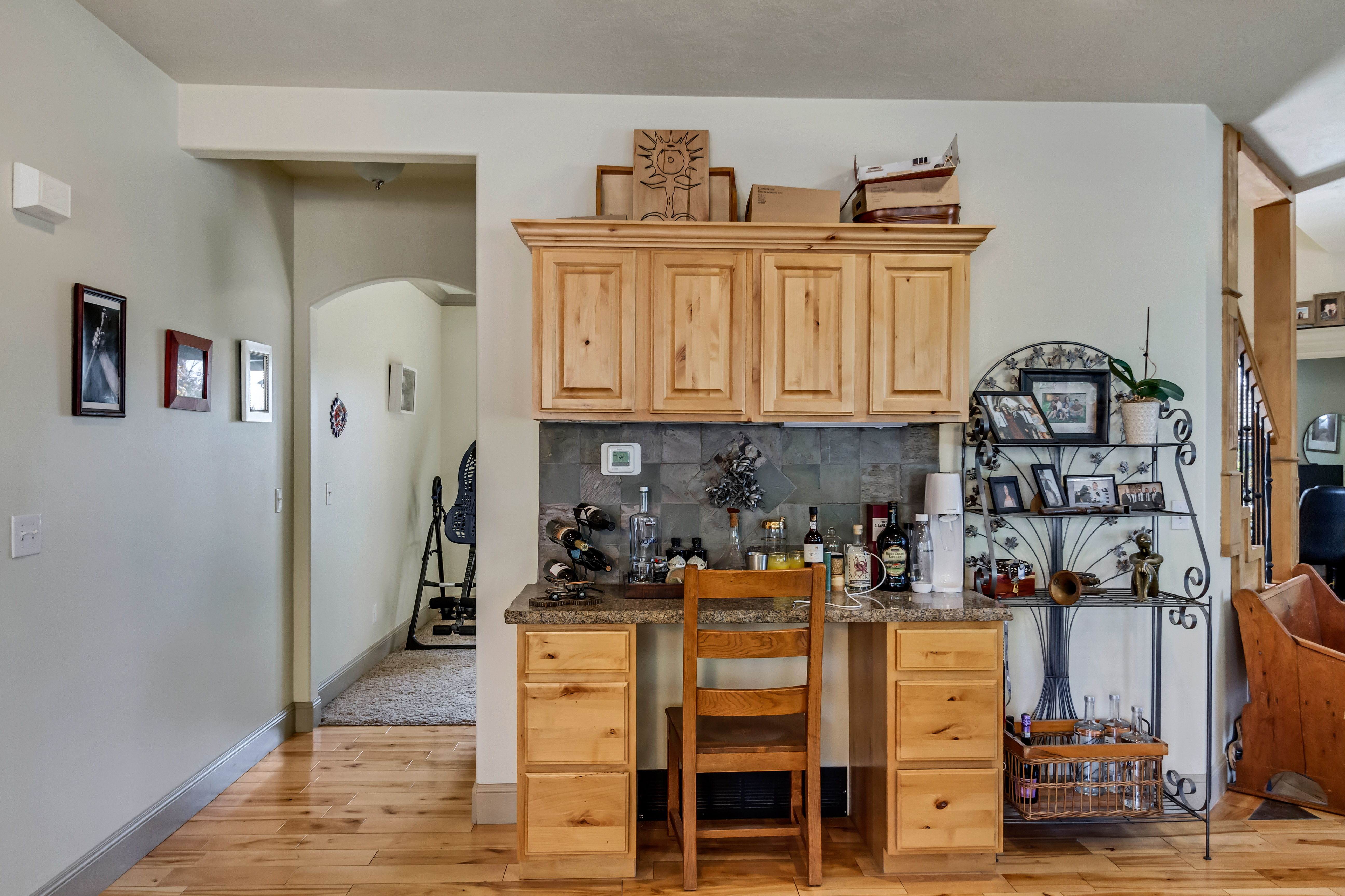 Built-in cabinetry with a stone-look backsplash, light wood-finish flooring, a built-in desk area with a granite-look countertop, and an arched hallway entry