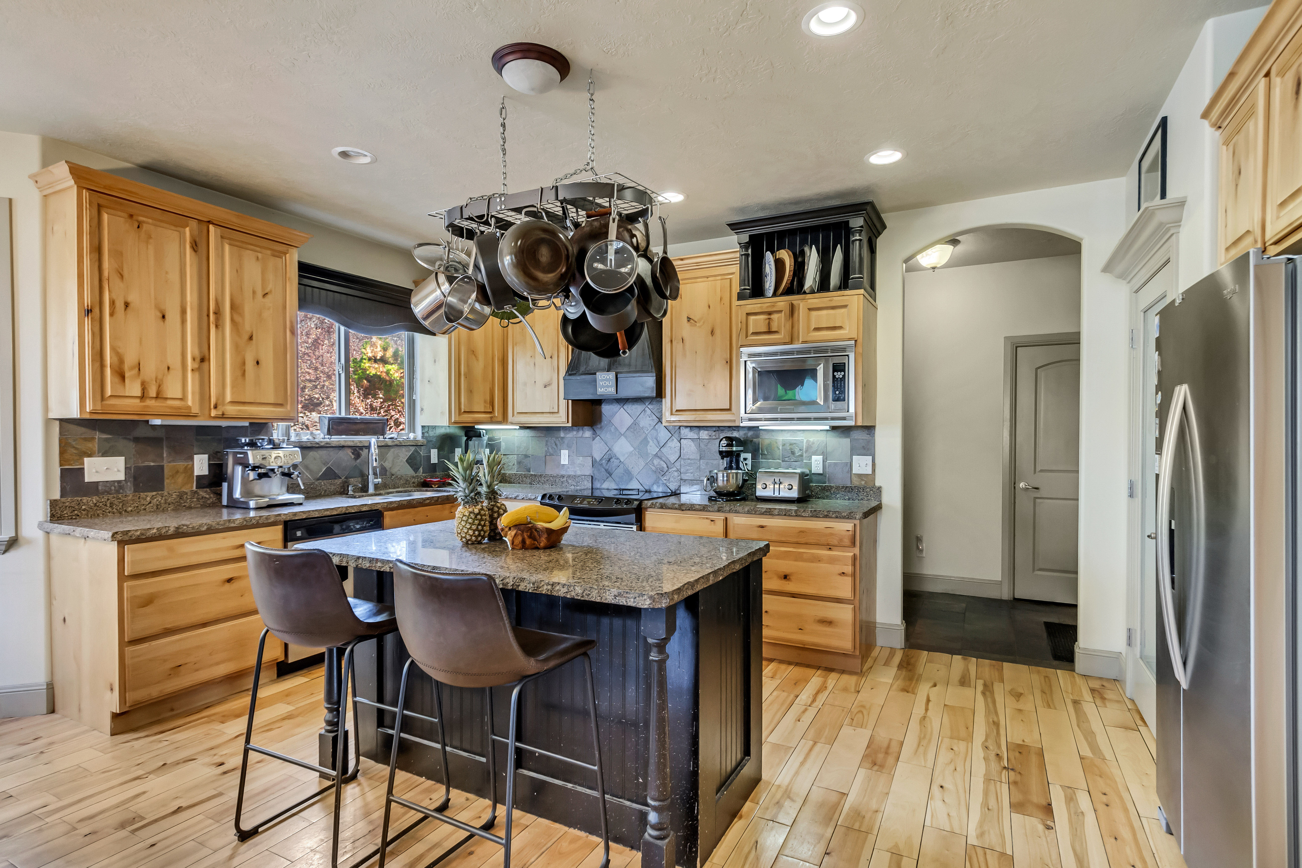 Kitchen featuring wood-finish flooring, natural wood cabinetry, a central island with a stone-finish countertop, stainless steel appliances, and a tiled backsplash