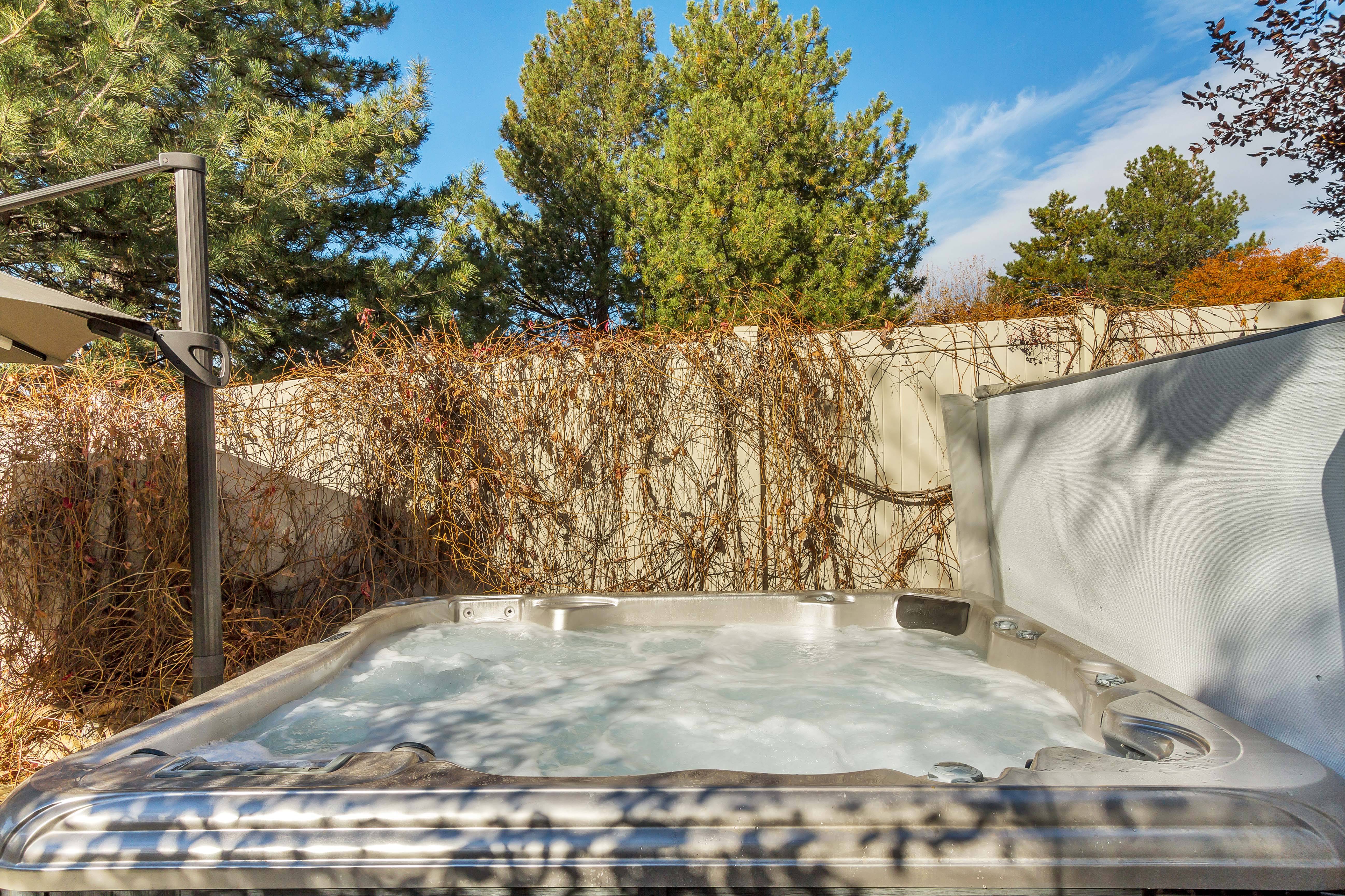 Outdoor spa with bubbling water, accompanied by a privacy wall and mature trees