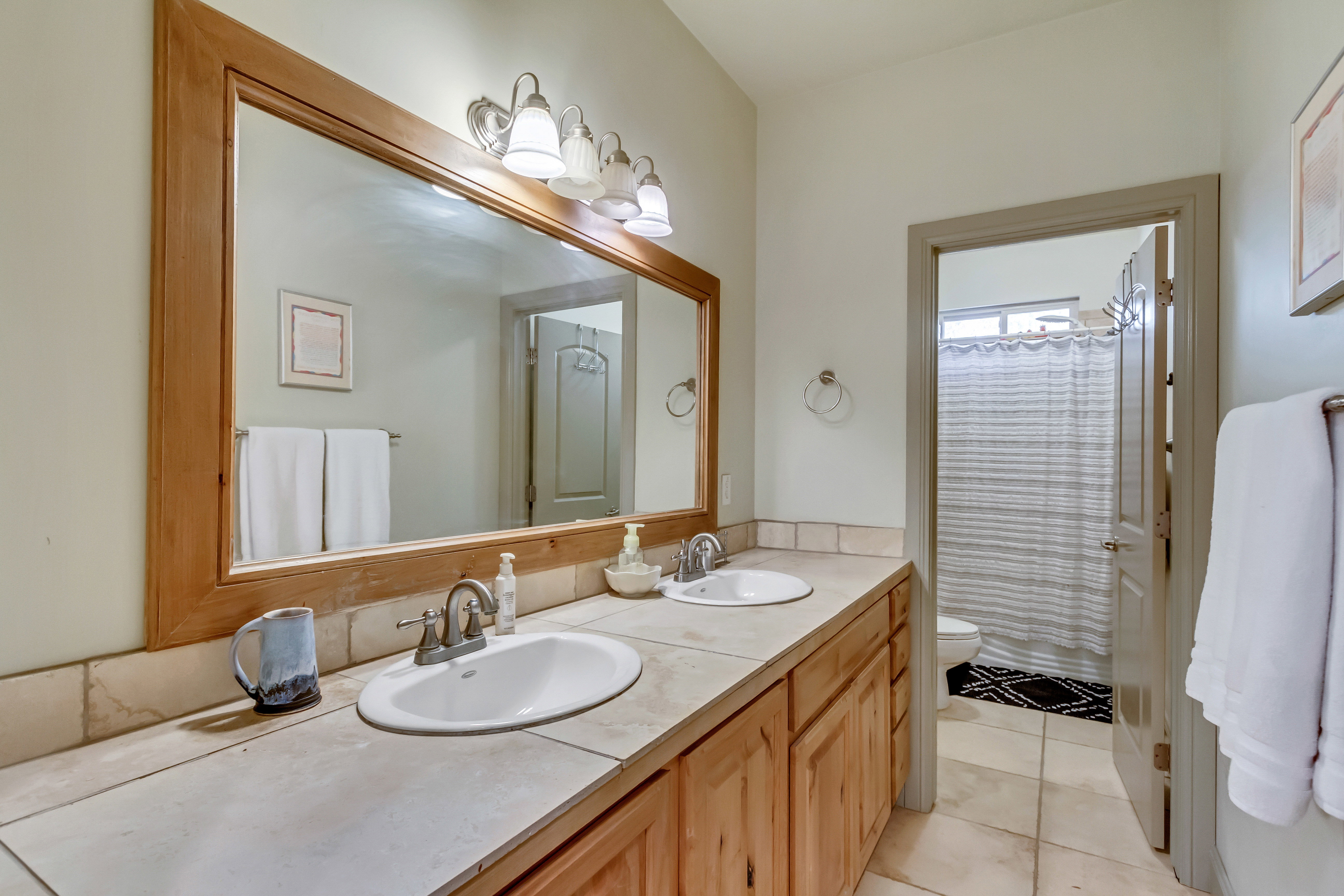 Dual vanity with tile countertop, wood-finish cabinetry, and framed mirror