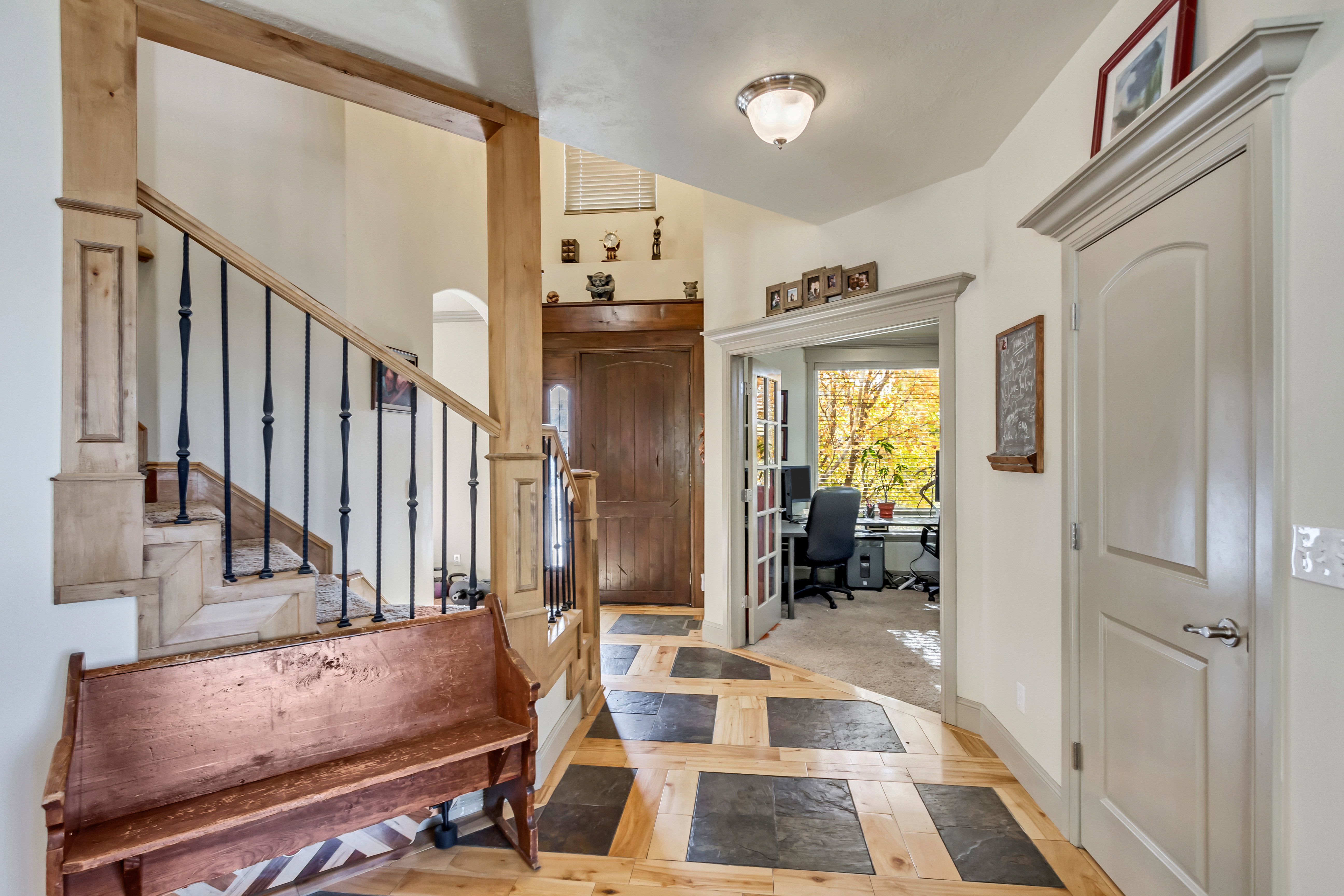 Entryway featuring a staircase with wood newel posts and black iron balusters, a mix of light wood and dark square tile flooring, a paneled door with decorative trim, and an arched doorway opening to an additional room