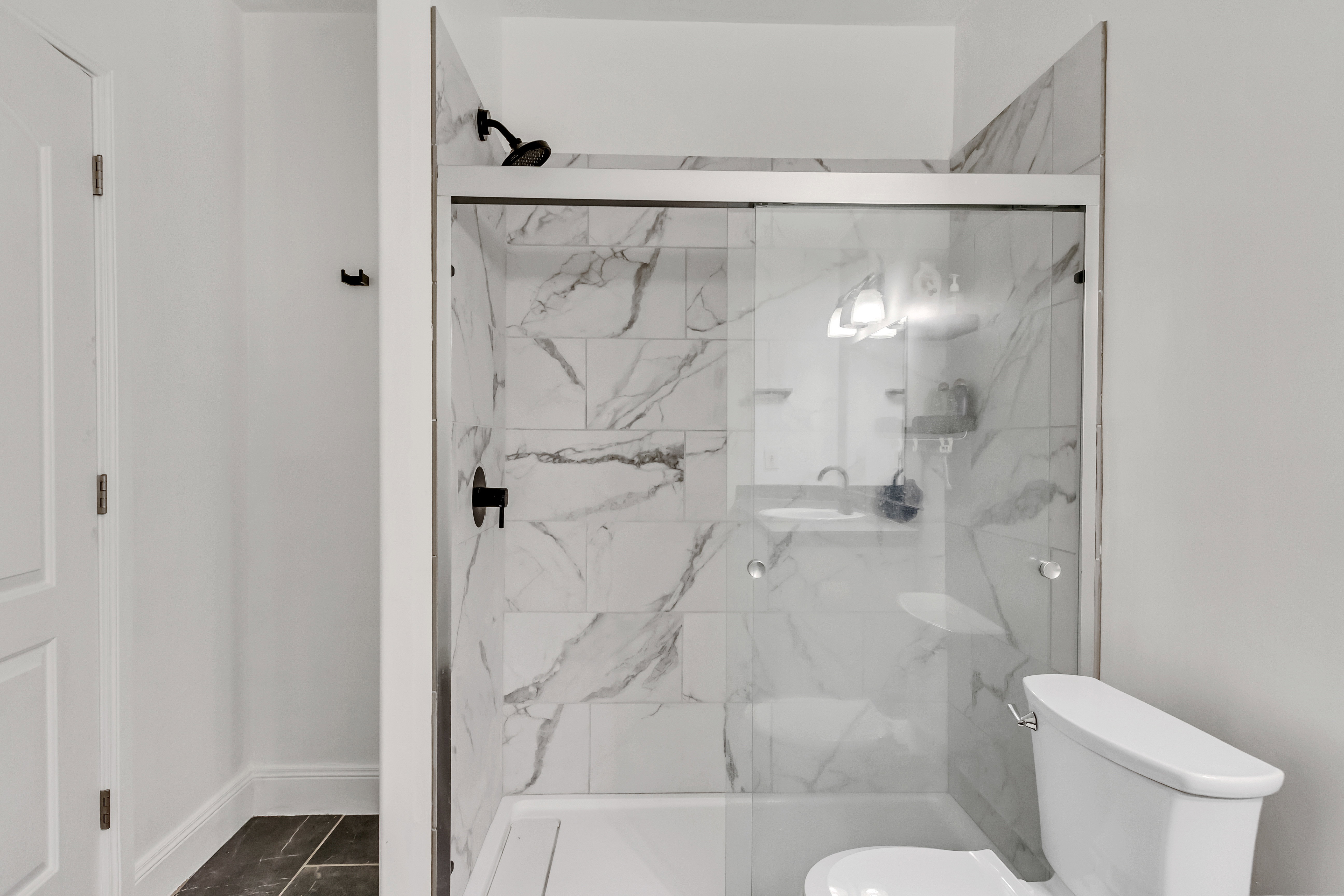 Shower with sliding glass doors, white subway tile surround with gray veining, matte black shower fixtures, and integrated shelving
