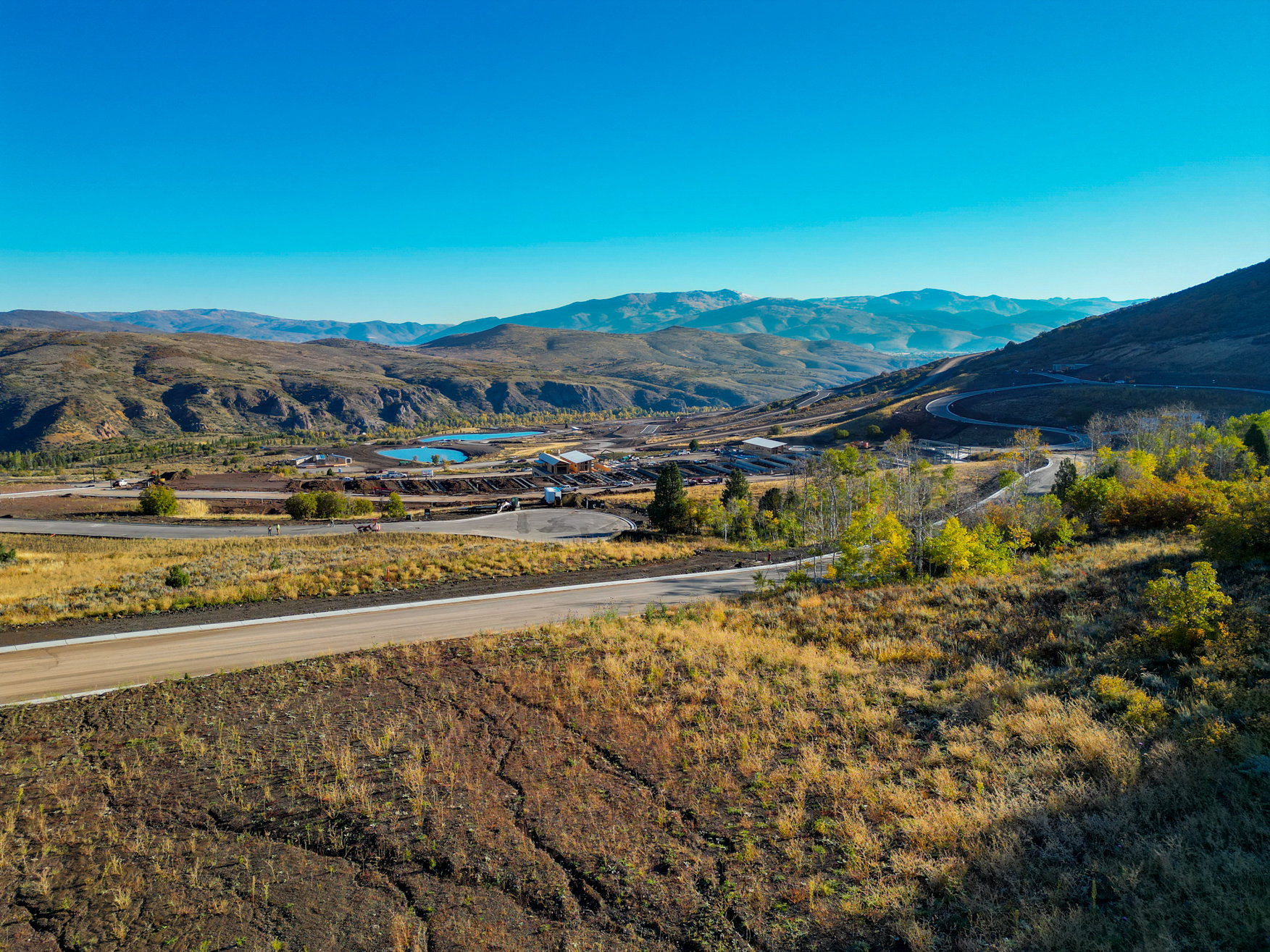 Expansive mountain landscape featuring a winding road, natural bodies of water, and distant structures