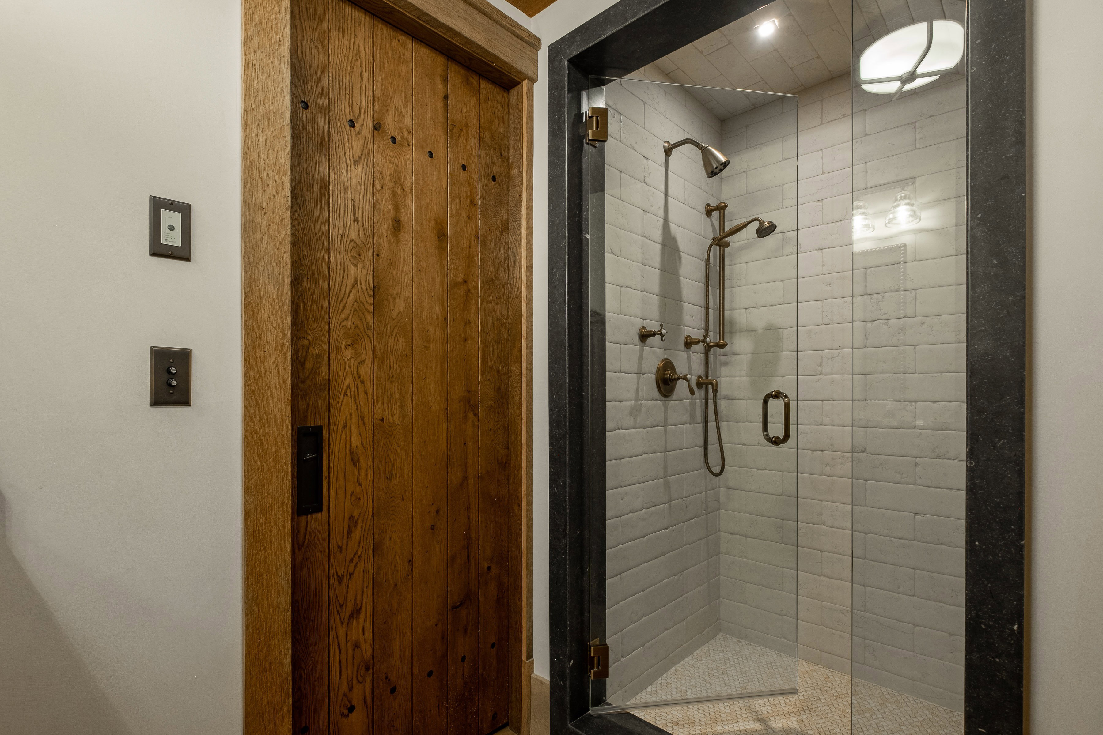 Walk-in shower featuring a frameless glass enclosure, subway tile surround, bronze-finish fixtures, and a pebble tile floor