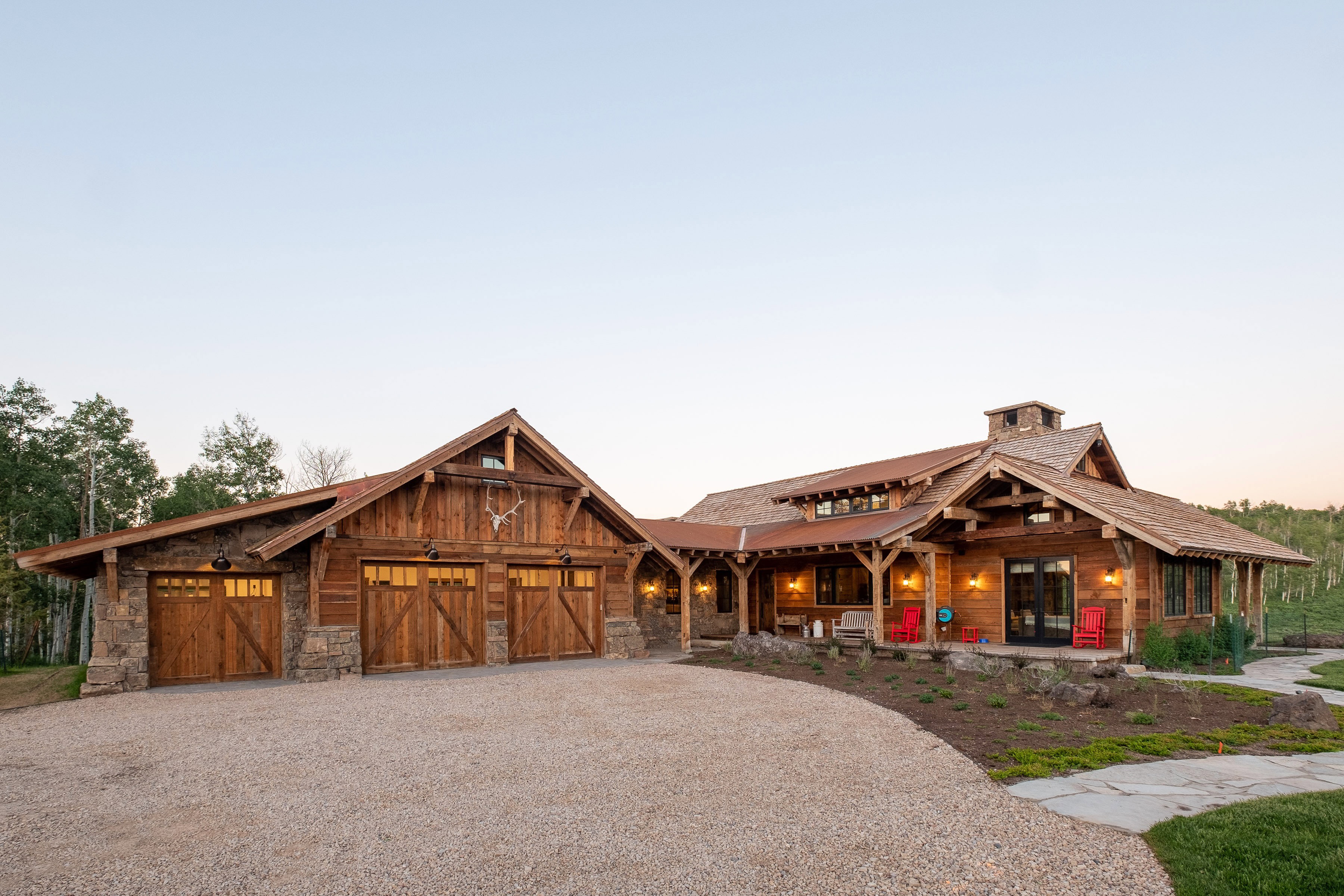 Rustic-style exterior featuring a gravel driveway, stone and wood siding, and a wooden three-car garage
