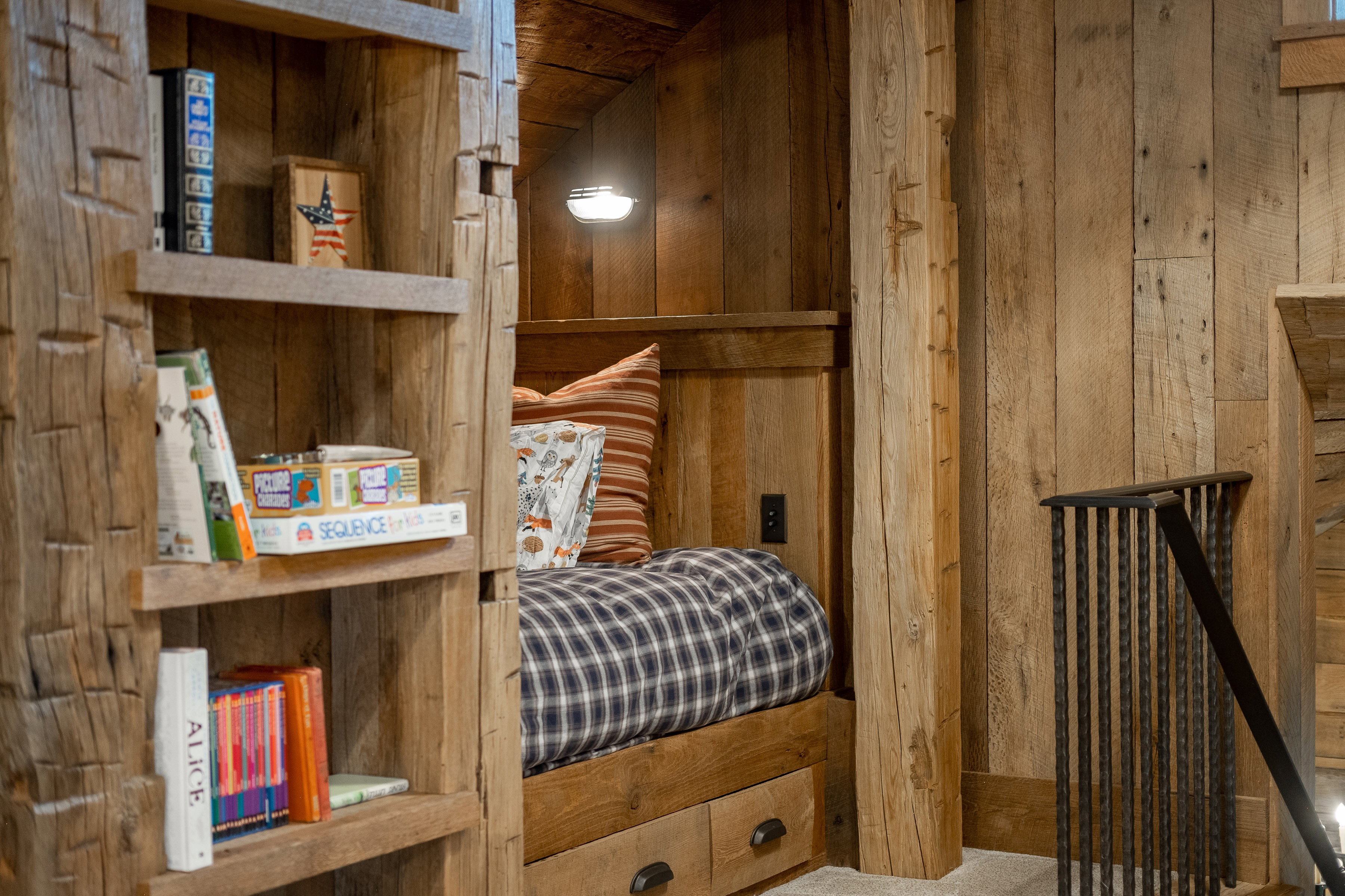 Built-in wood-paneled sleeping nook featuring a wall-mounted light fixture, integrated storage drawers, and adjacent custom shelving