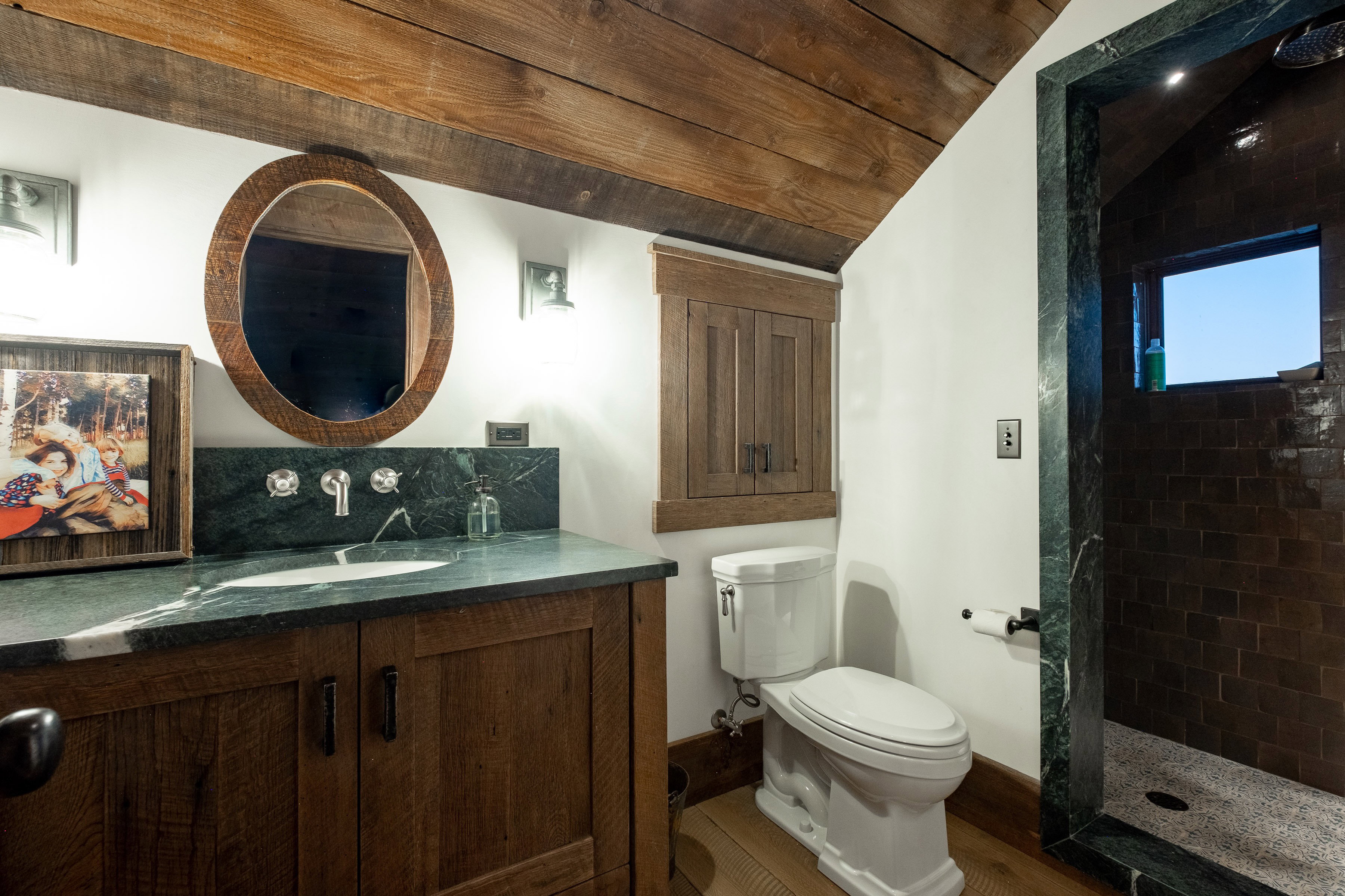 Bathroom featuring a wood-finish vanity with an integrated sink, a dark stone countertop and backsplash, and wall-mounted fixtures