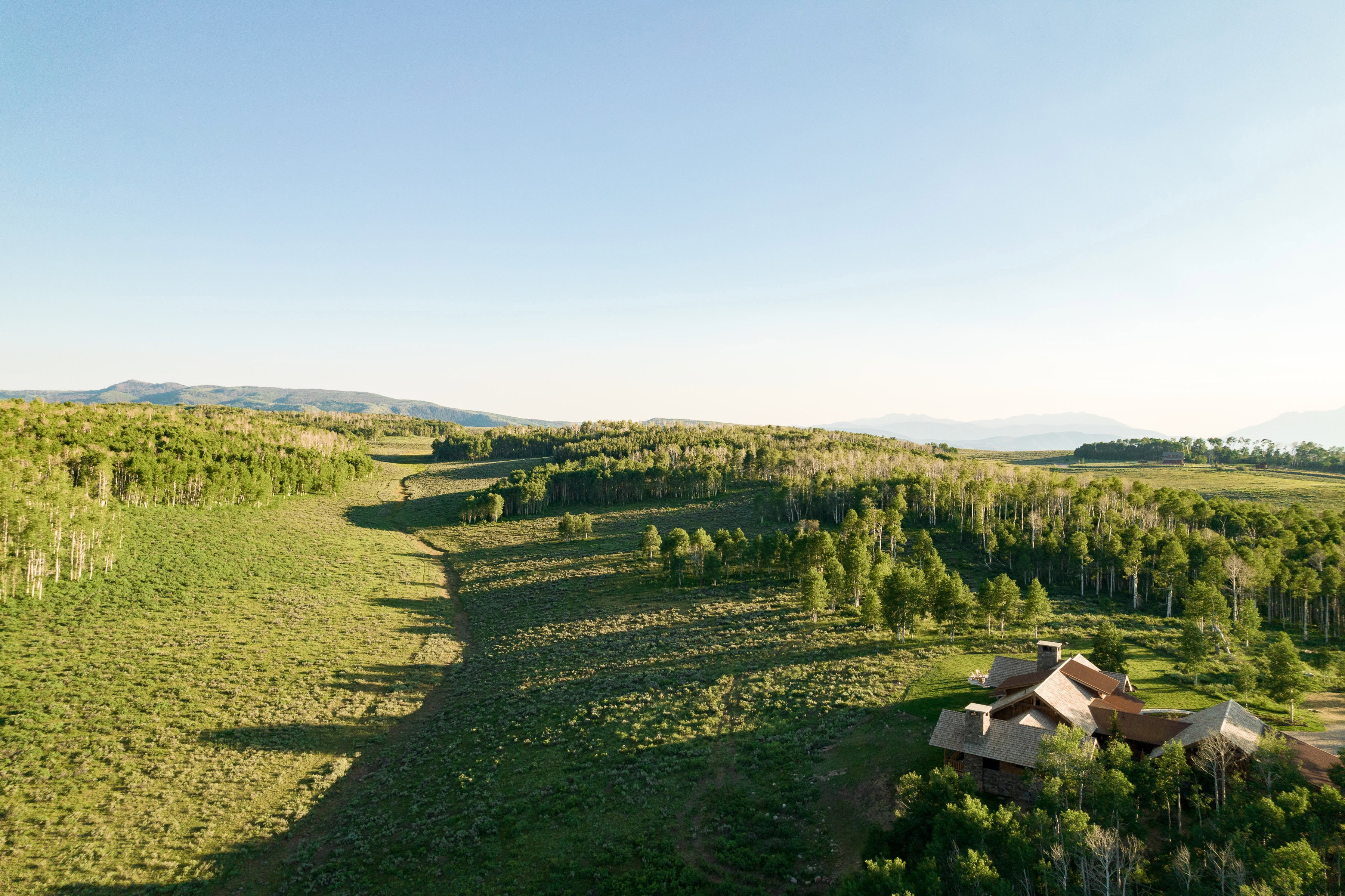 Expansive rural landscape featuring a single-family residence with multiple gables and dormers, surrounded by abundant mature trees and rolling hills