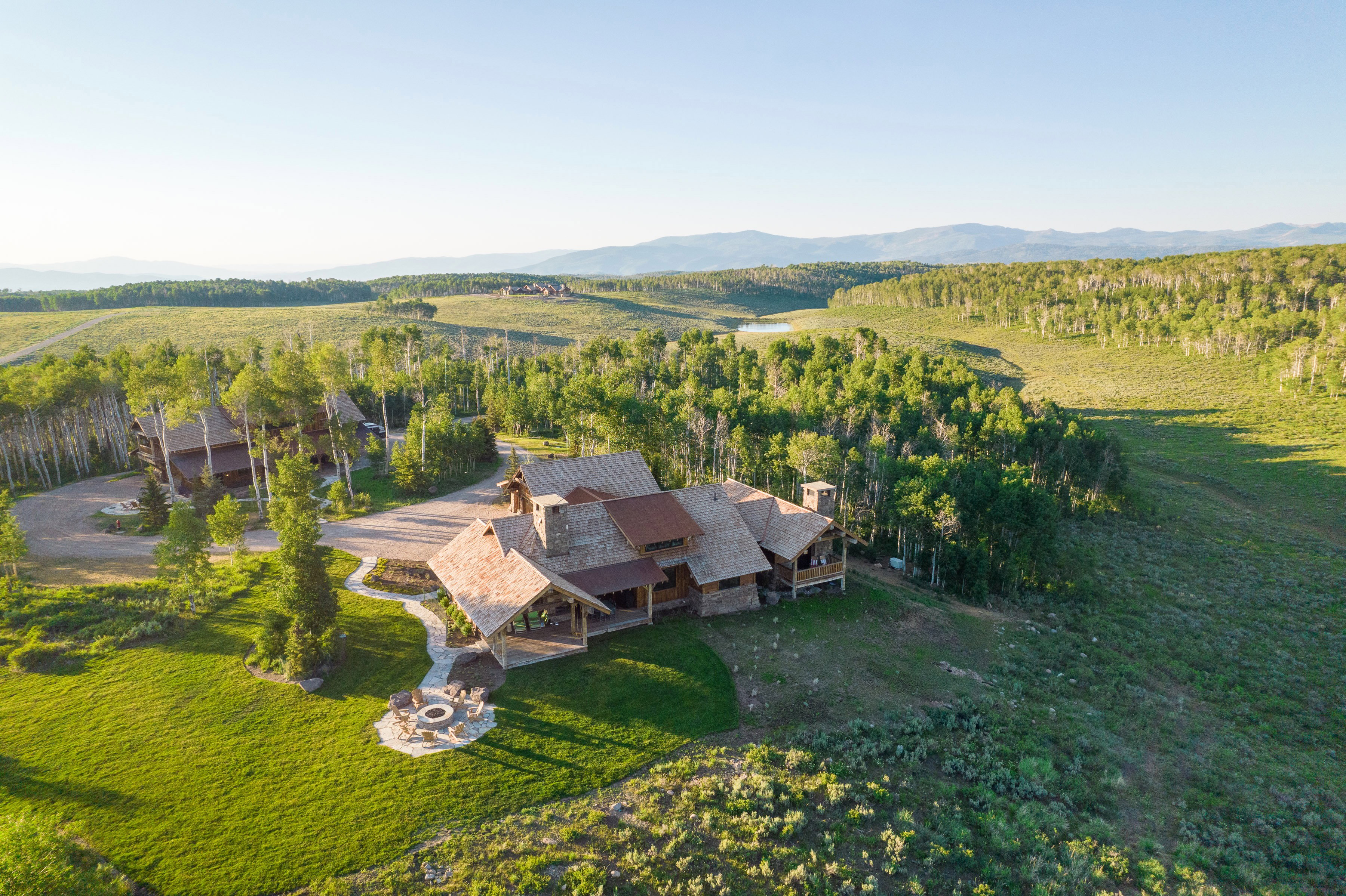 Expansive property featuring a rustic-style residence, mature trees, a stone fire pit, extensive green space, and a distant mountain range